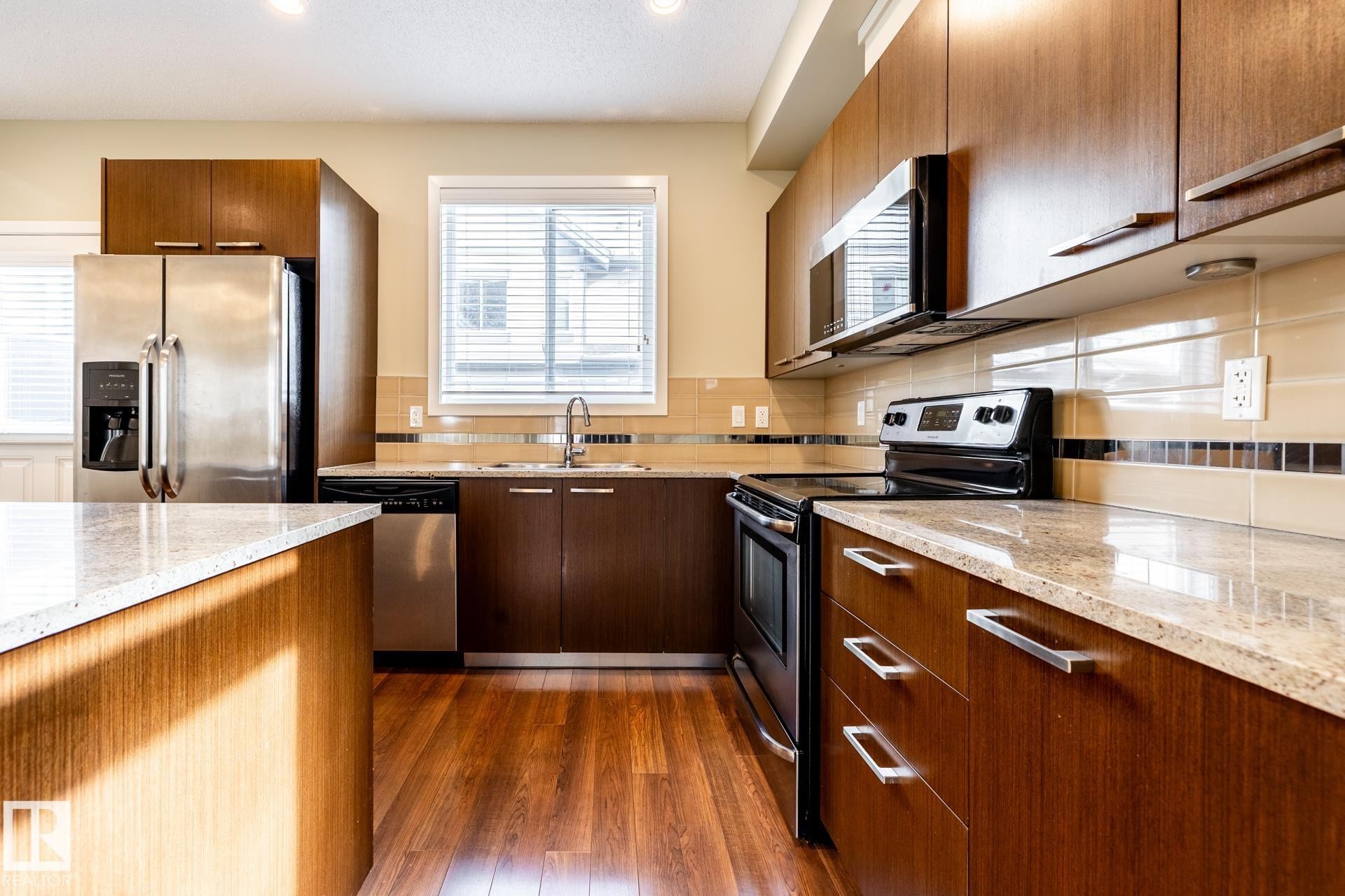 Kitchen with stainless steel appliances, light stone counters, dark wood finished floors, wood finish cabinetry, and recessed lighting - 21 655 Watt Boulevard, Edmonton, AB - Indoor Photo Showing Kitchen