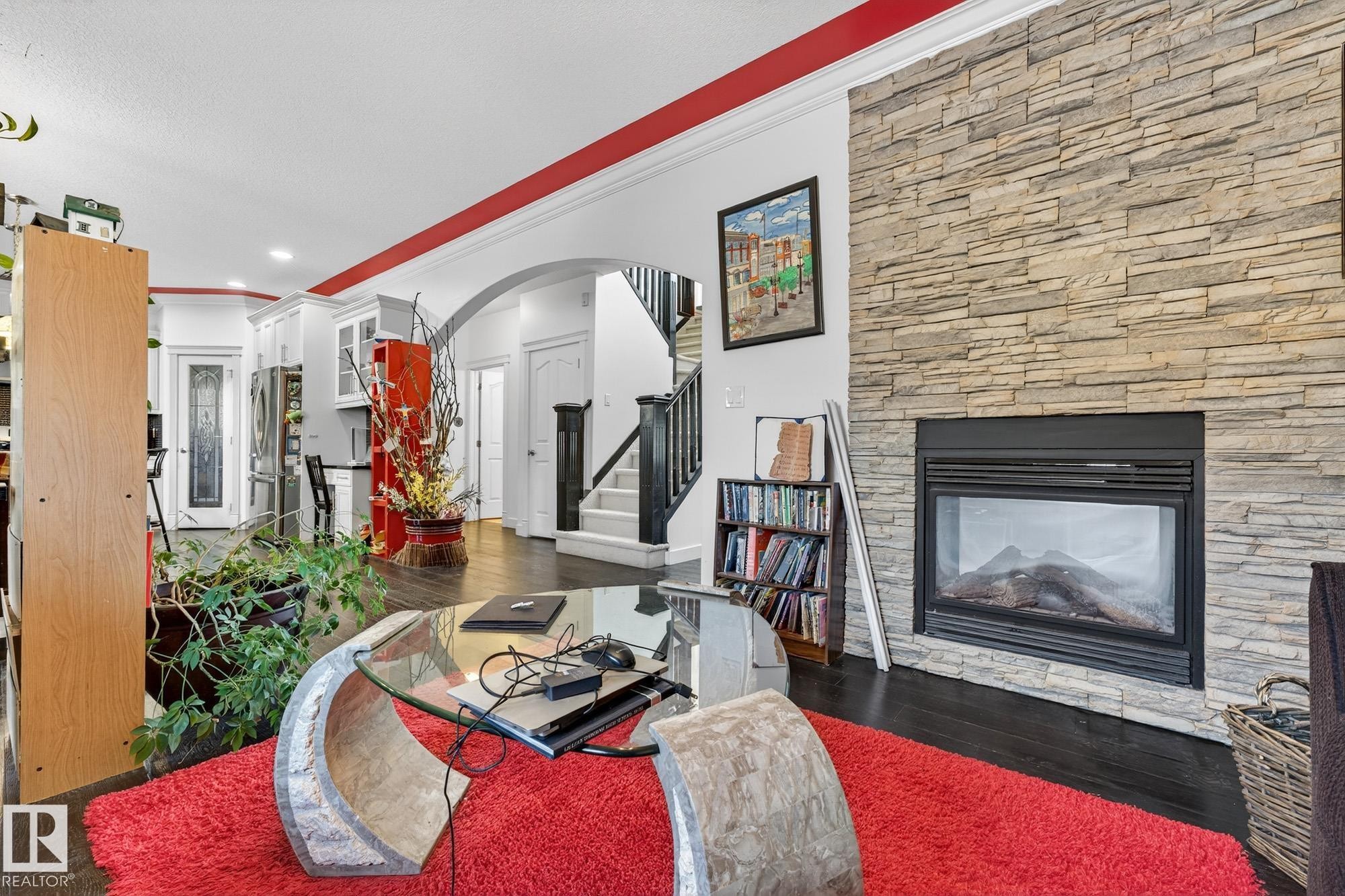 Living area with arched walkways, crown molding, a stone fireplace, dark wood-style floors, and recessed lighting - 1660 Malone Way, Edmonton, AB - Indoor Photo Showing Living Room With Fireplace