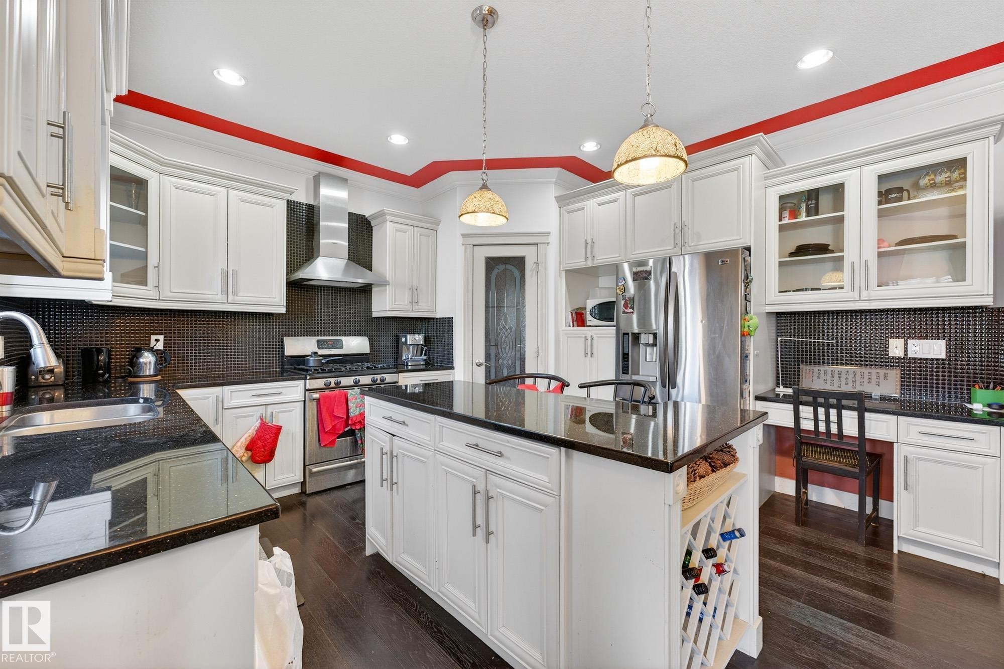 Kitchen with glass insert cabinets, decorative backsplash, stainless steel appliances, dark wood-style floors, and ornamental molding - 1660 Malone Way, Edmonton, AB - Indoor Photo Showing Kitchen With Upgraded Kitchen