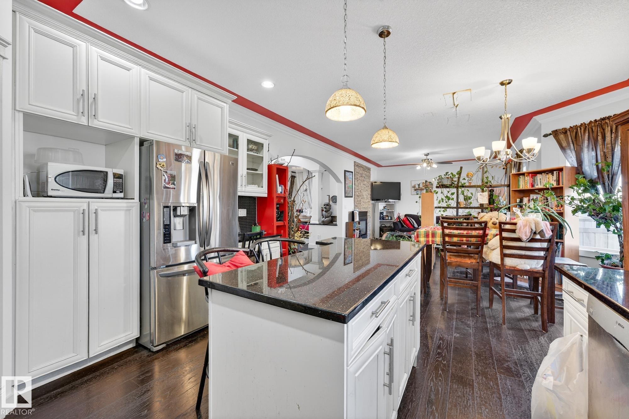 Kitchen with white cabinets, stainless steel appliances, hanging lights, dark stone countertops, and a ceiling fan - 1660 Malone Way, Edmonton, AB - Indoor Photo Showing Kitchen With Upgraded Kitchen