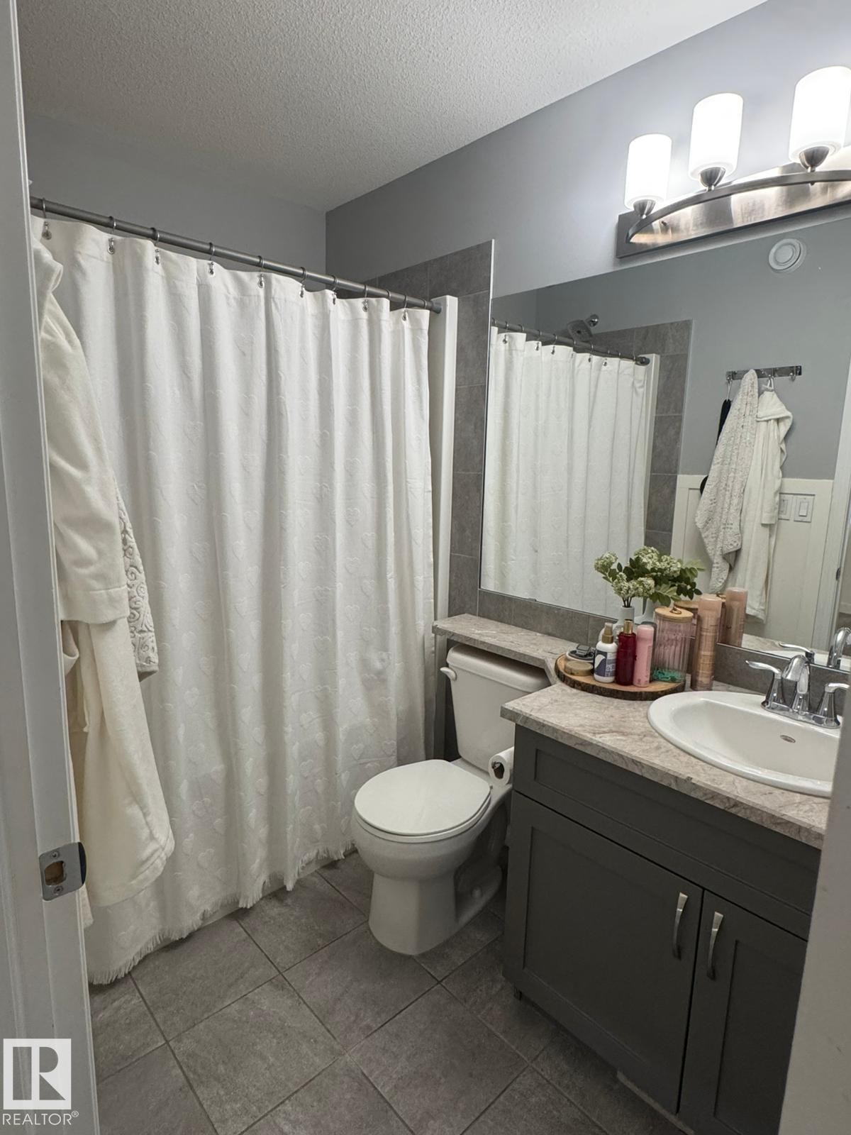 Full bathroom featuring vanity, a textured ceiling, a shower with shower curtain, and dark tile patterned floors - 17703 65 Street, Edmonton, AB - Indoor Photo Showing Bathroom