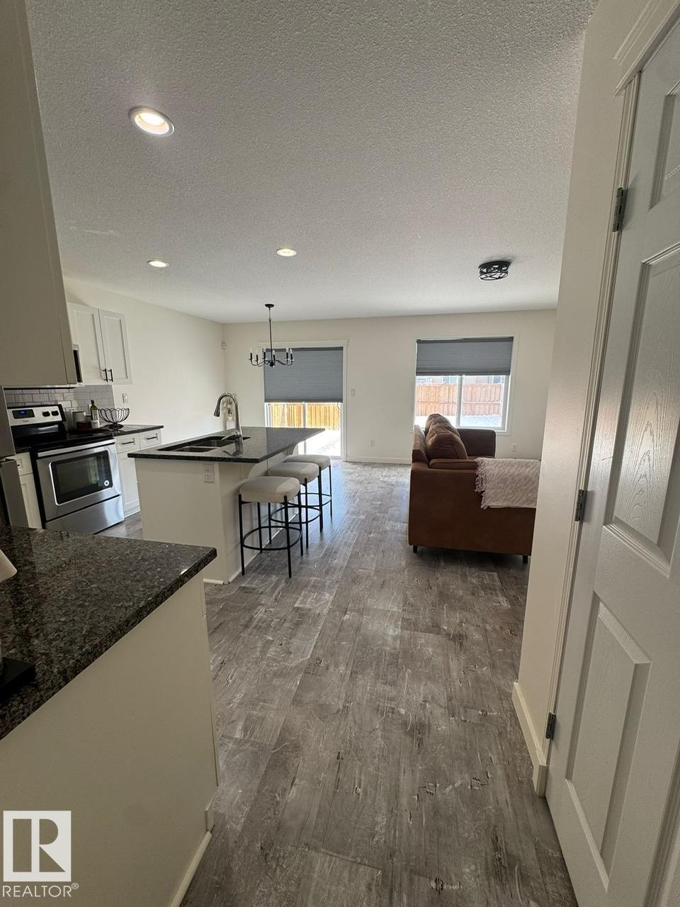 Kitchen with a kitchen bar, an island with sink, electric stove, white cabinetry, and a textured ceiling - 17703 65 Street, Edmonton, AB - Indoor Photo Showing Other Room