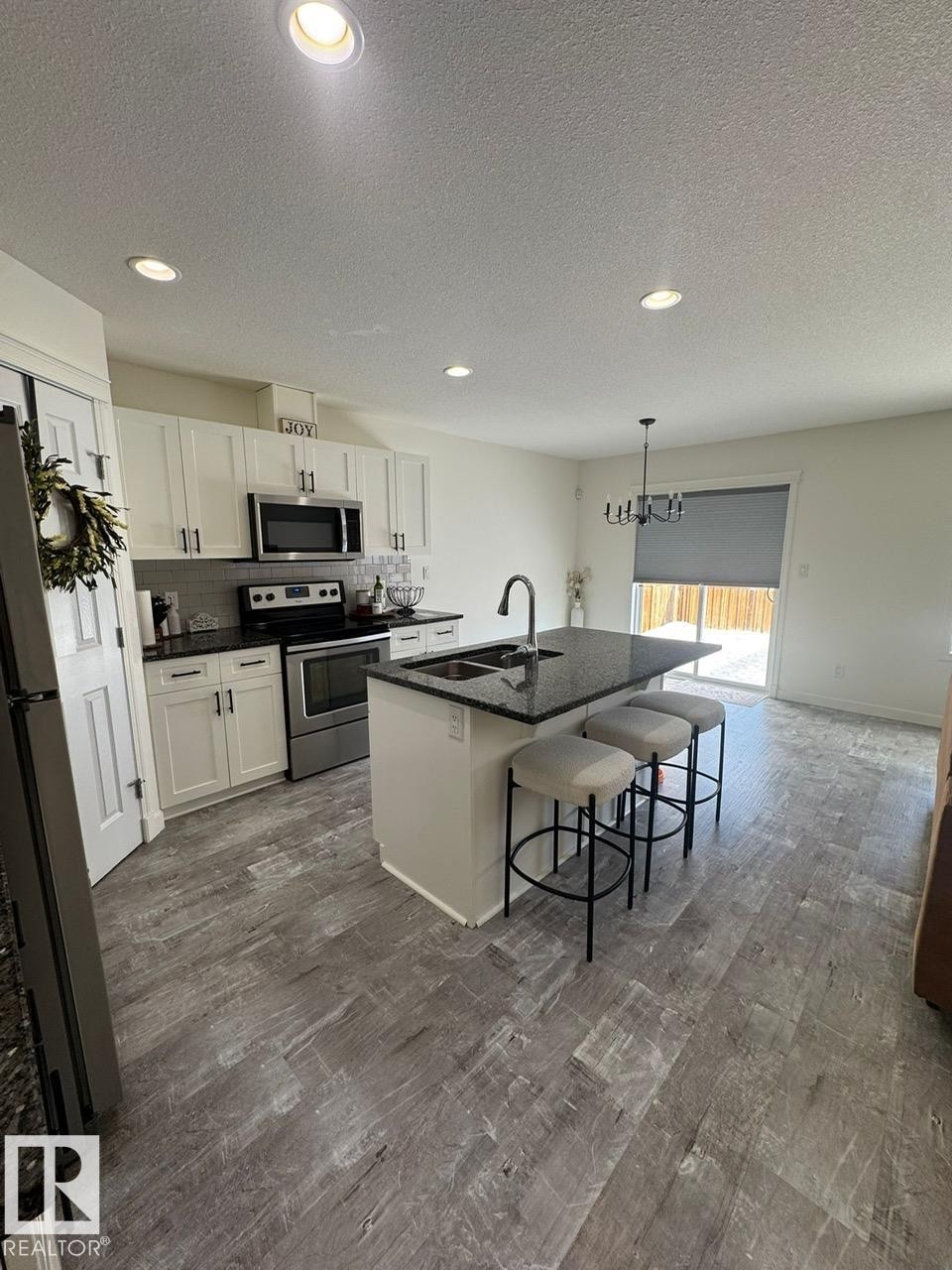 Kitchen with stainless steel appliances, a textured ceiling, white cabinets, an island with sink, and a kitchen breakfast bar - 17703 65 Street, Edmonton, AB - Indoor Photo Showing Kitchen
