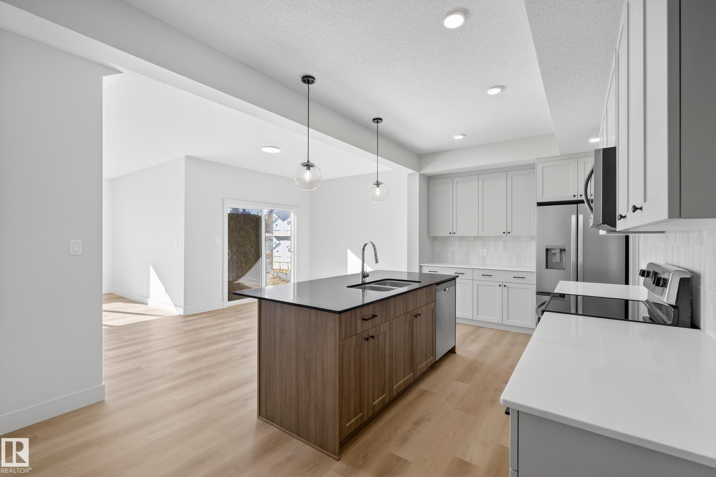 Two tone kitchen featuring two tone cabinetry, stainless steel appliances, an island with sink, light wood-style floors, and dark stone countertops - 22 Grayson Green, Stony Plain, AB - Indoor Photo Showing Kitchen With Double Sink With Upgraded Kitchen
