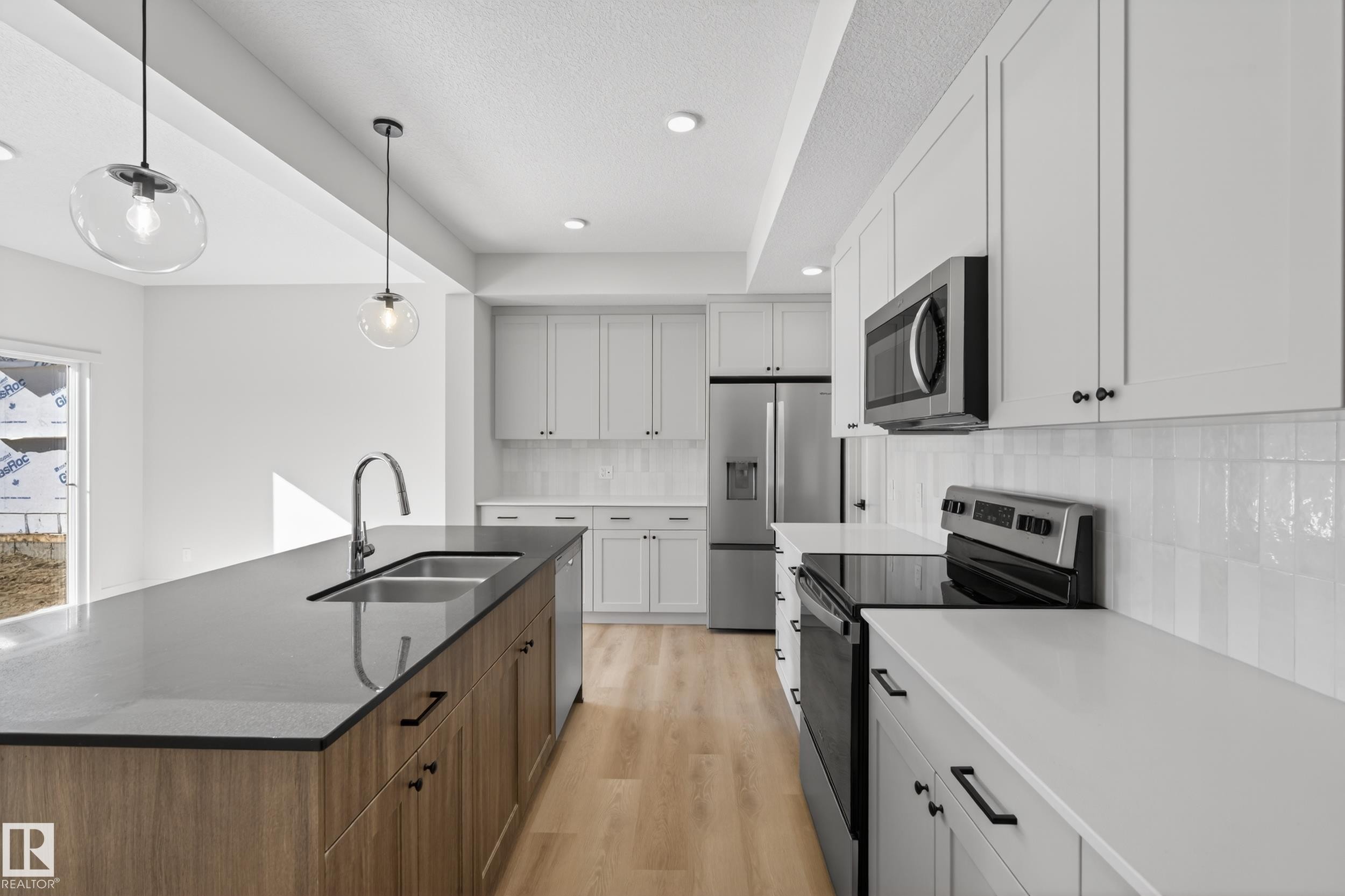 Two tone kitchen featuring stainless steel appliances, two tone cabinetry, light wood-style flooring, dark stone countertops, and a center island with sink - 22 Grayson Green, Stony Plain, AB - Indoor Photo Showing Kitchen With Double Sink With Upgraded Kitchen