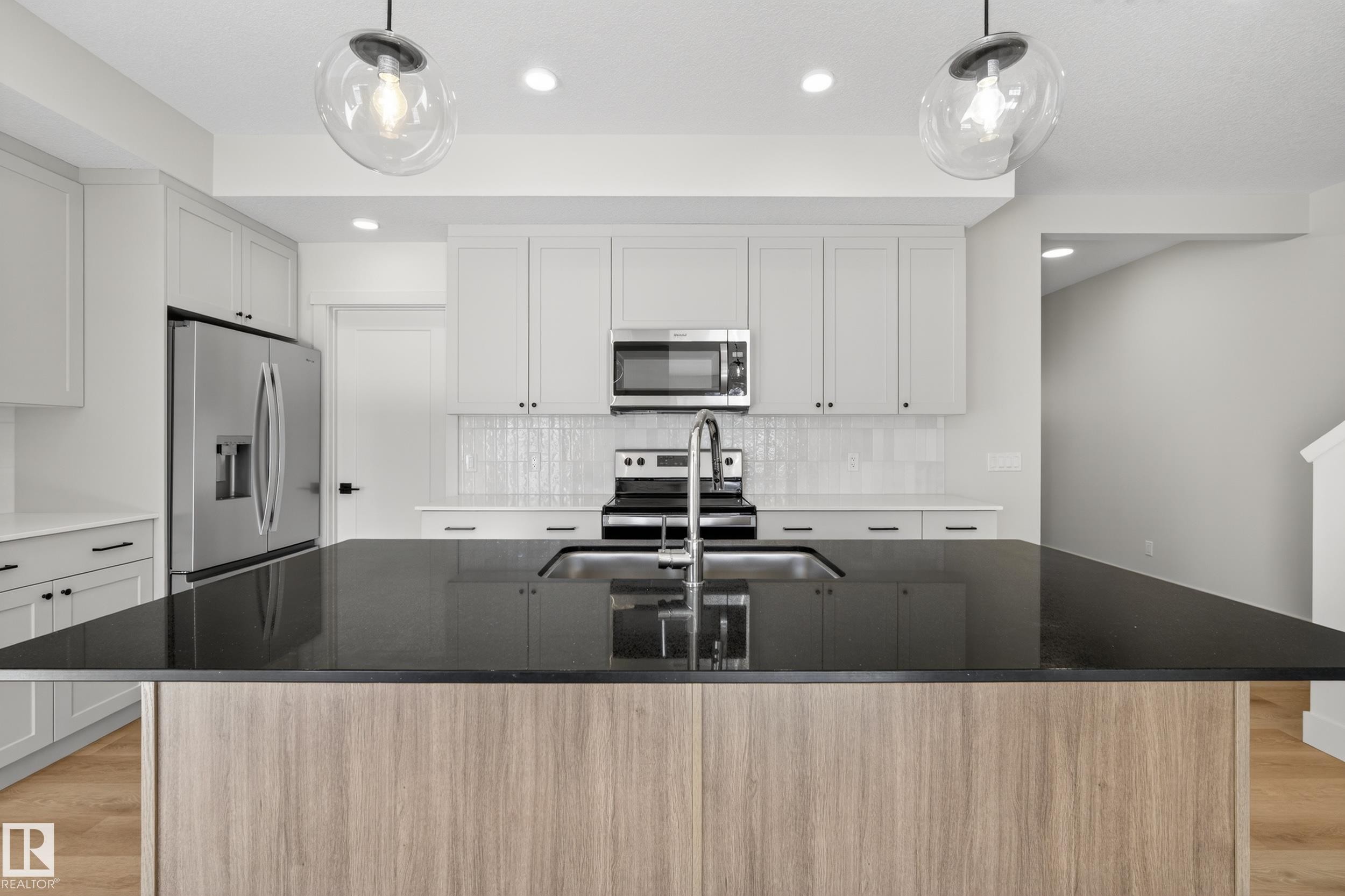 Kitchen featuring light wood-style floors, dark stone countertops, stainless steel appliances, and a kitchen island with sink - 22 Grayson Green, Stony Plain, AB - Indoor Photo Showing Kitchen With Upgraded Kitchen
