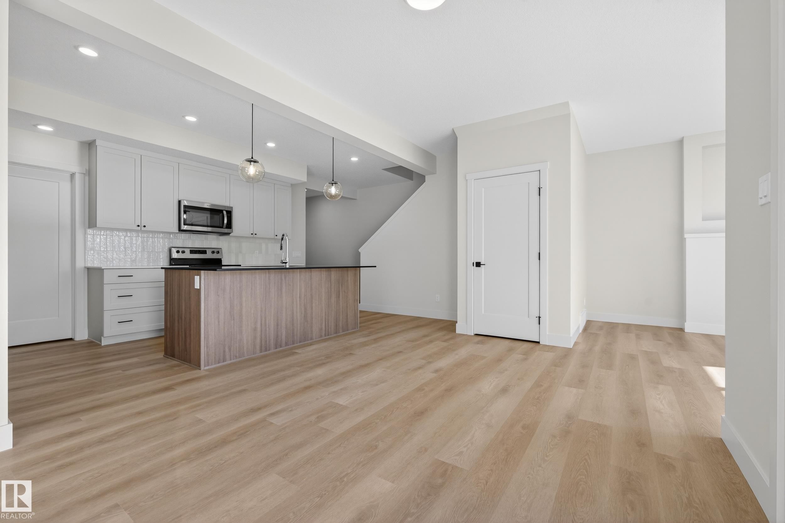 Two tone kitchen with an island with sink, two tone cabinets, light wood-style flooring, decorative light fixtures, and backsplash - 22 Grayson Green, Stony Plain, AB - Indoor Photo Showing Kitchen