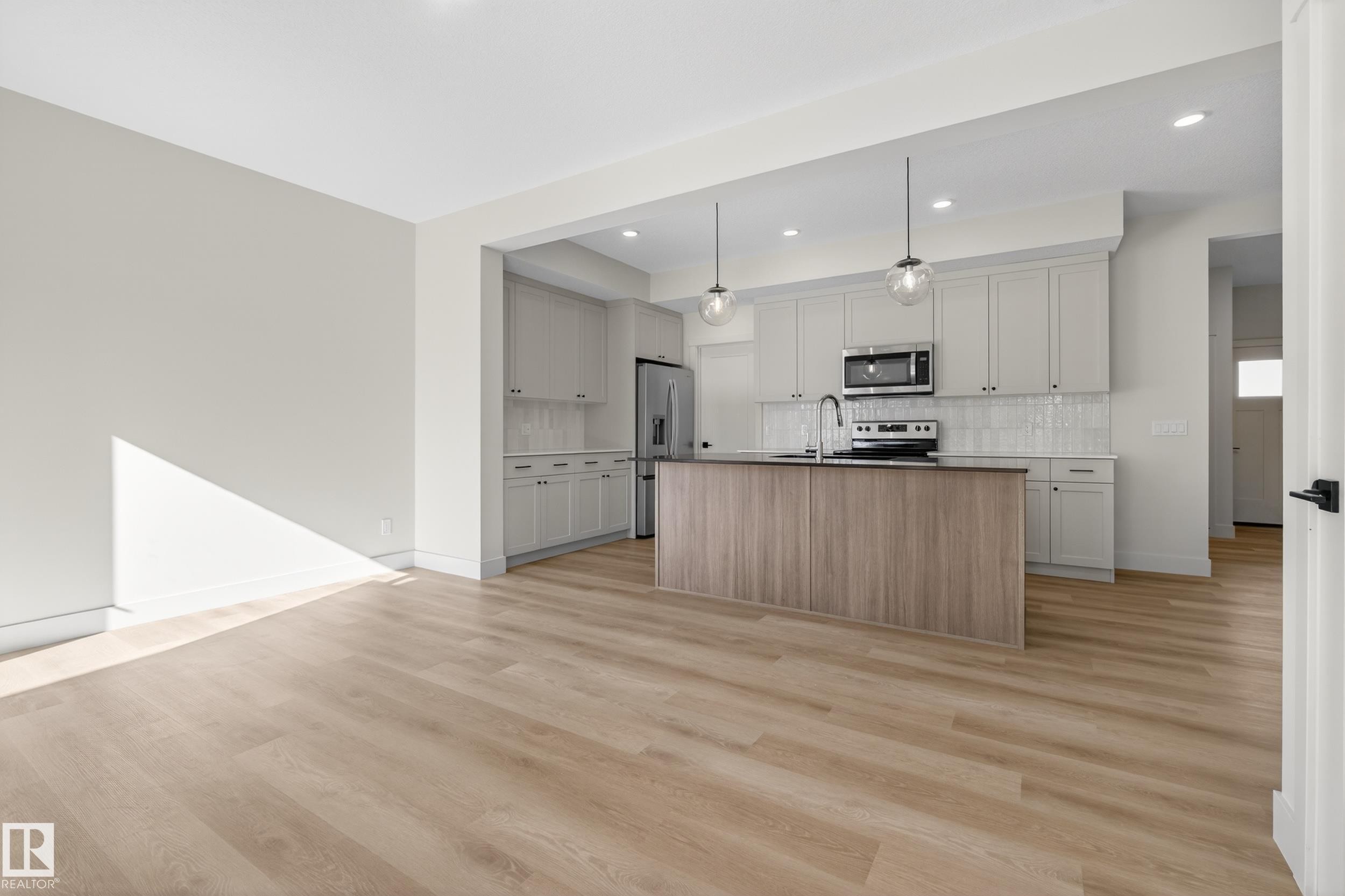 Dual tone kitchen with a center island with sink, stainless steel appliances, open floor plan, light wood finished floors, and decorative backsplash - 22 Grayson Green, Stony Plain, AB - Indoor Photo Showing Kitchen With Upgraded Kitchen