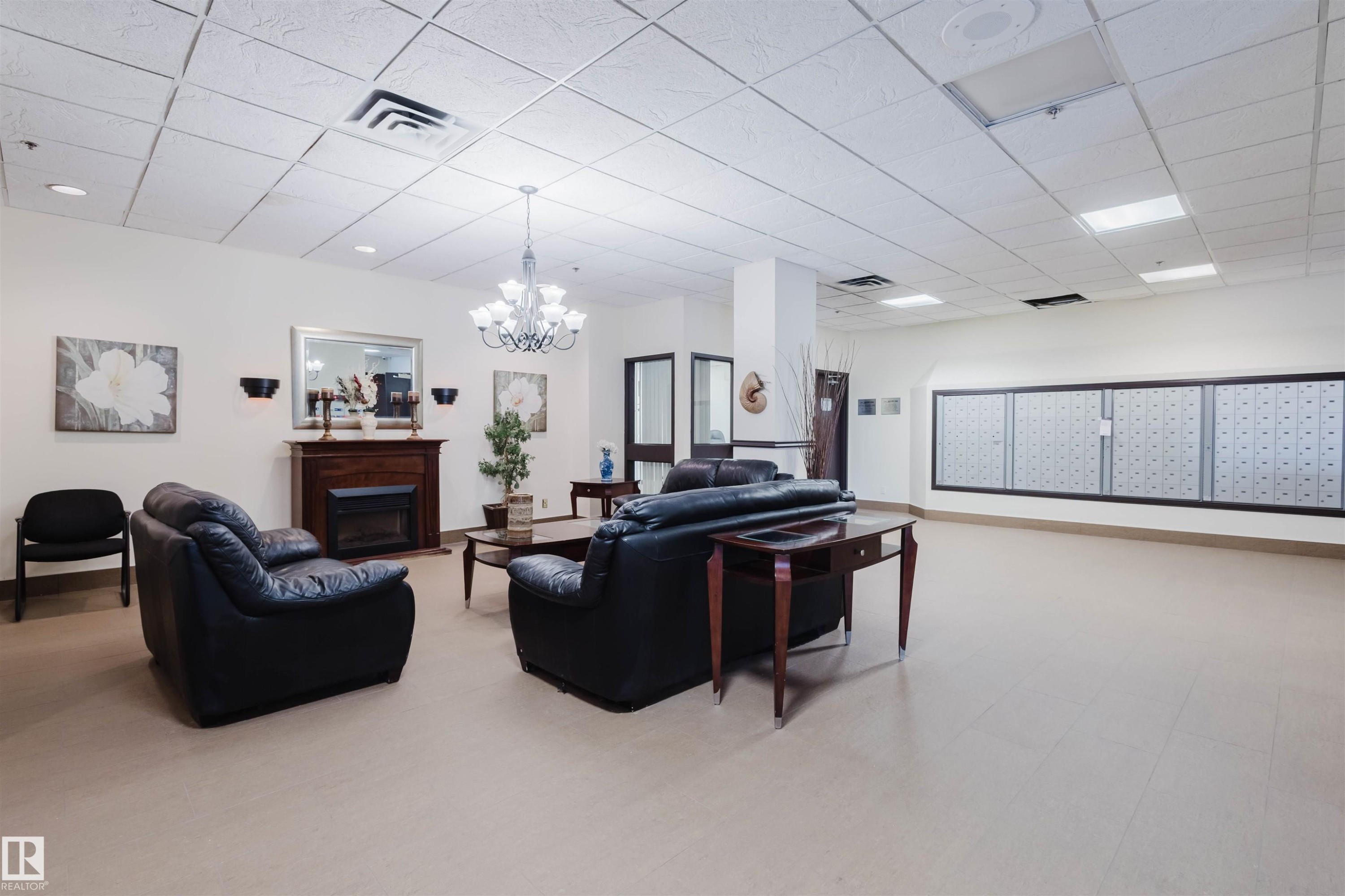 Living room featuring a drop ceiling, mail area, a fireplace, light flooring, and a chandelier - 1803 10149 Saskatchewan Drive, Edmonton, AB - Indoor