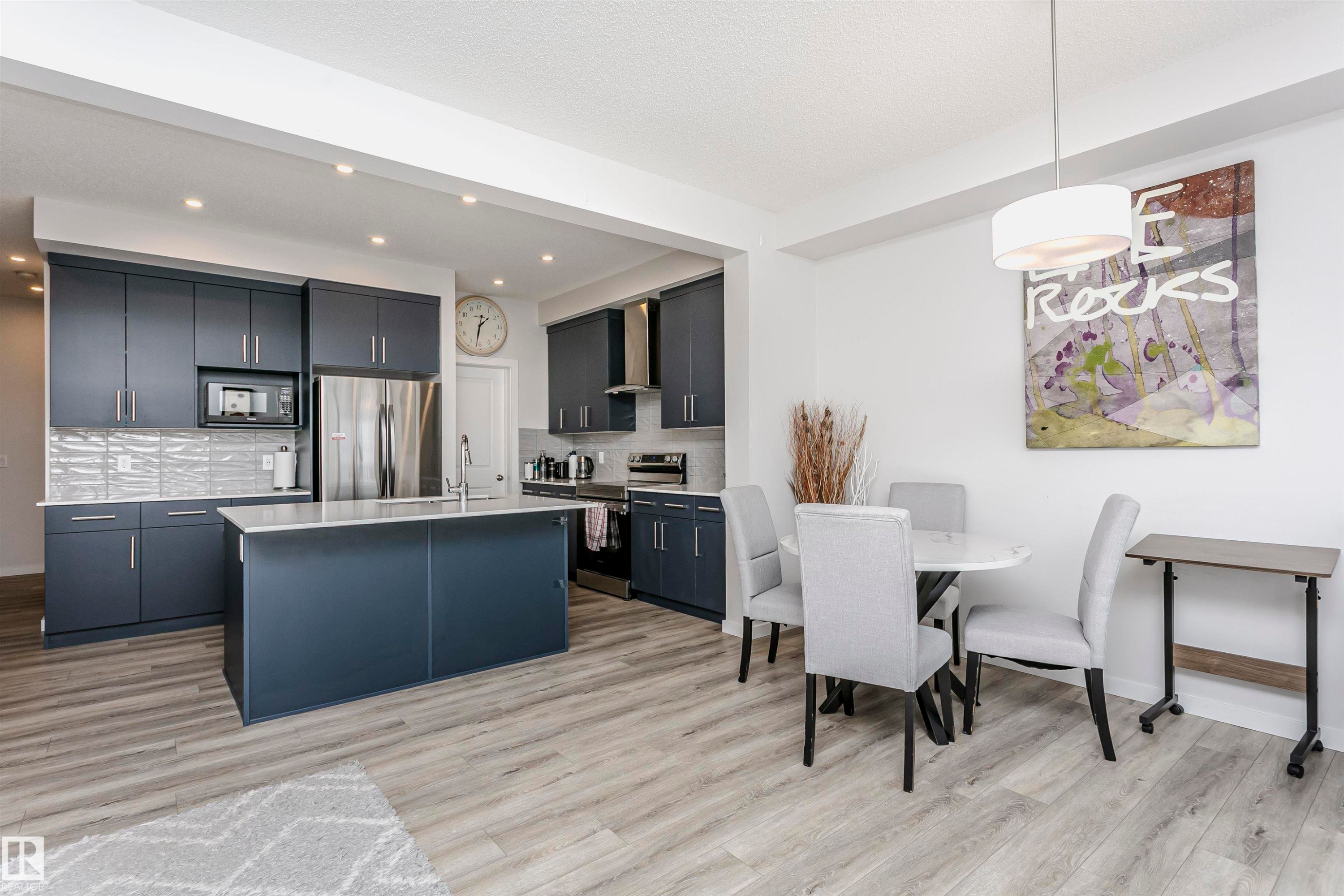 Kitchen with an island with sink, appliances with stainless steel finishes, decorative light fixtures, decorative backsplash, and light wood-style flooring - 9421 Pear Crescent, Edmonton, AB - Indoor