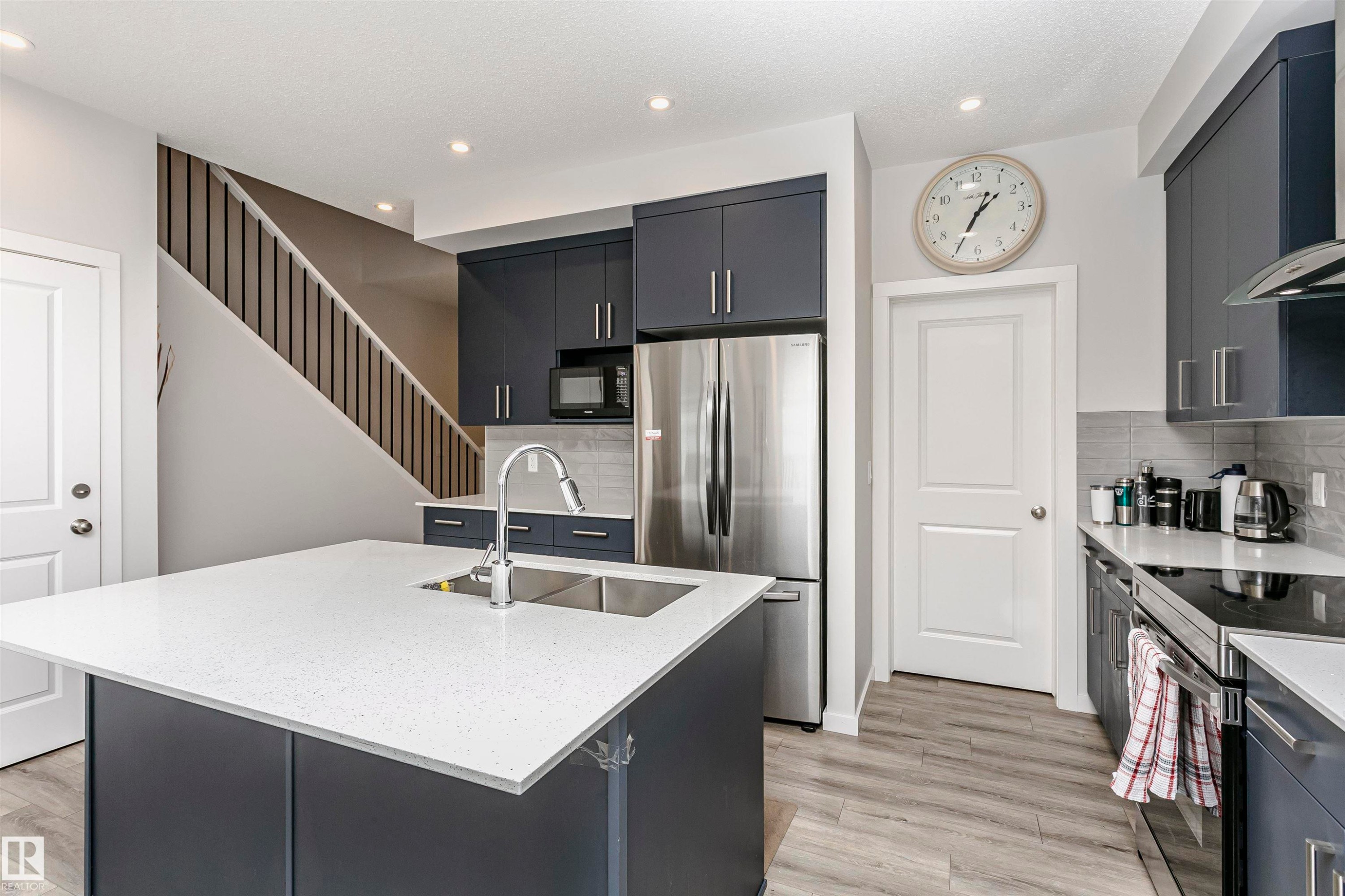 Kitchen with stainless steel appliances, light stone counters, a kitchen island with sink, dark cabinets, and wall chimney range hood - 9421 Pear Crescent, Edmonton, AB - Indoor Photo Showing Kitchen With Stainless Steel Kitchen With Double Sink With Upgraded Kitchen