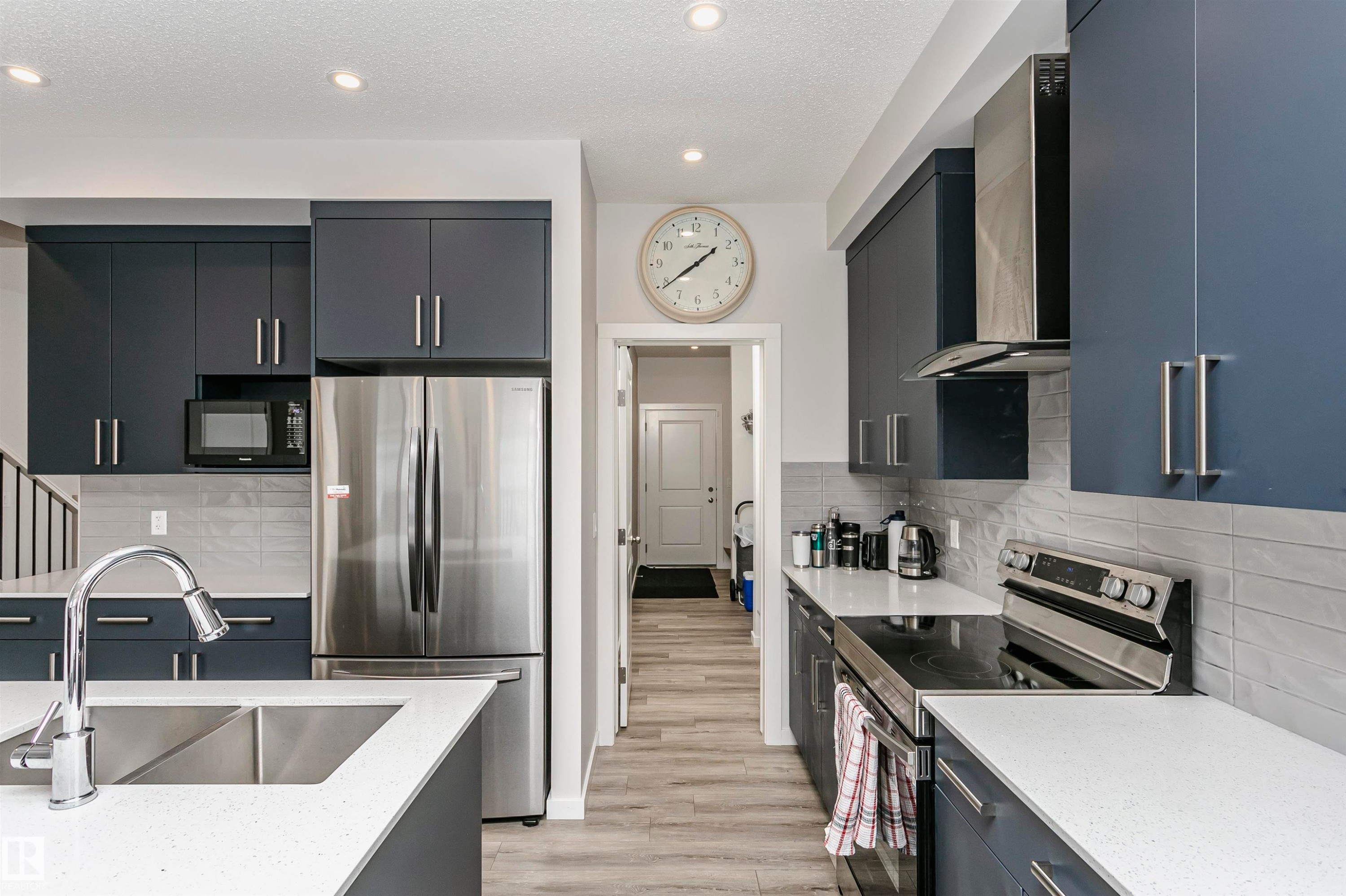 Kitchen featuring appliances with stainless steel finishes, decorative backsplash, a textured ceiling, light stone countertops, and wall chimney exhaust hood - 9421 Pear Crescent, Edmonton, AB - Indoor Photo Showing Kitchen With Stainless Steel Kitchen With Upgraded Kitchen