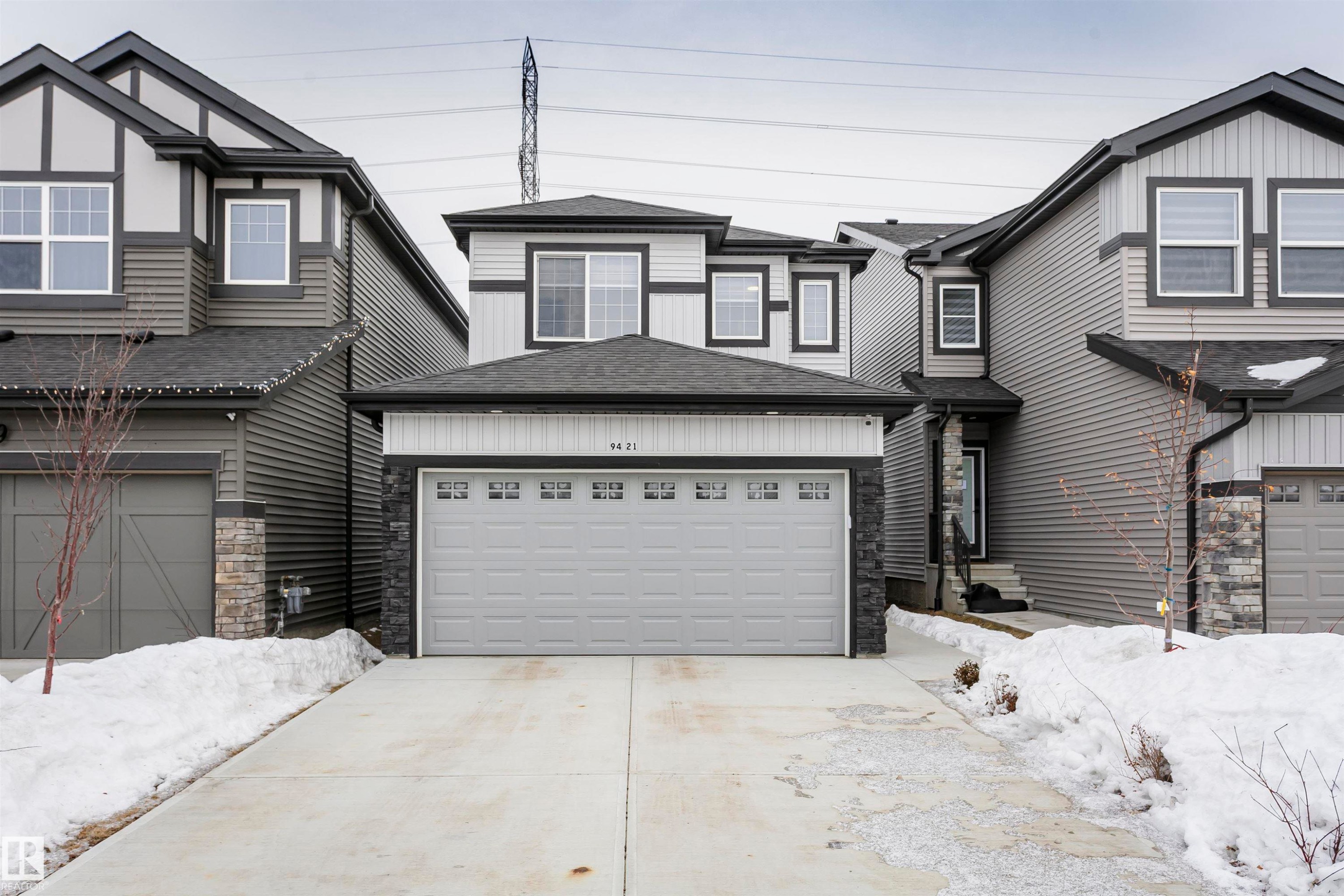 View of front of property featuring stone siding, concrete driveway, a shingled roof, and an attached garage - 9421 Pear Crescent, Edmonton, AB - Outdoor