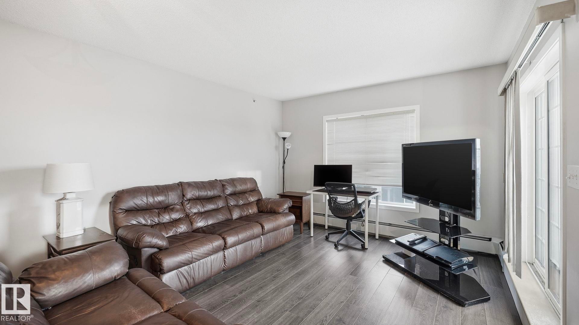 Living area featuring a desk, wood finished floors, and baseboard heating - 401 636 Mcallister Loop, Edmonton, AB - Indoor