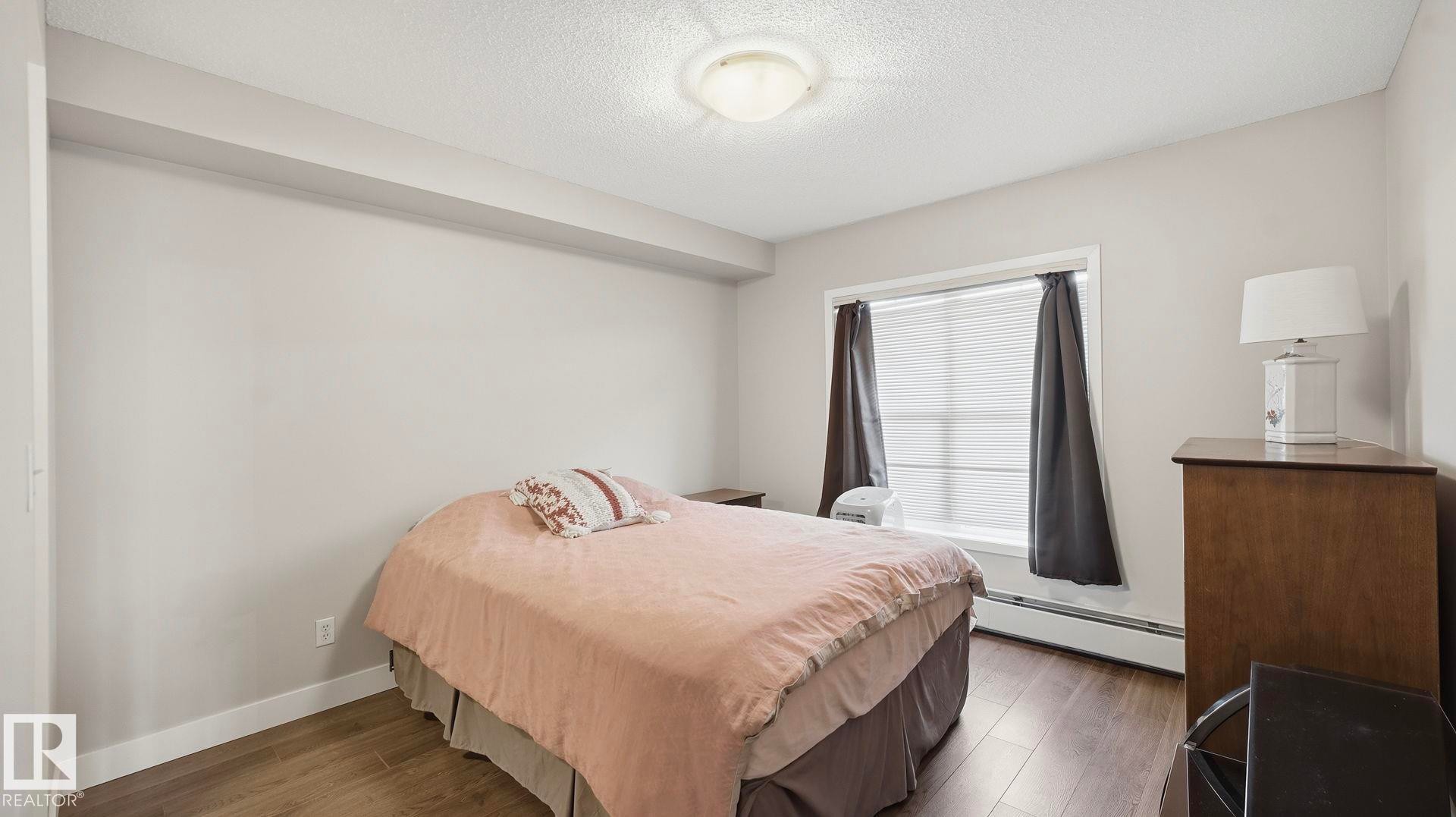 Bedroom with baseboard heating, dark wood finished floors, and a textured ceiling - 401 636 Mcallister Loop, Edmonton, AB - Indoor Photo Showing Bedroom