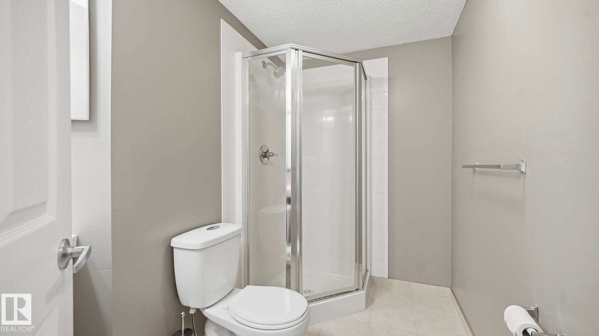 Bathroom with a shower stall, a textured ceiling, and light tile patterned floors - 401 636 Mcallister Loop, Edmonton, AB - Indoor Photo Showing Bathroom