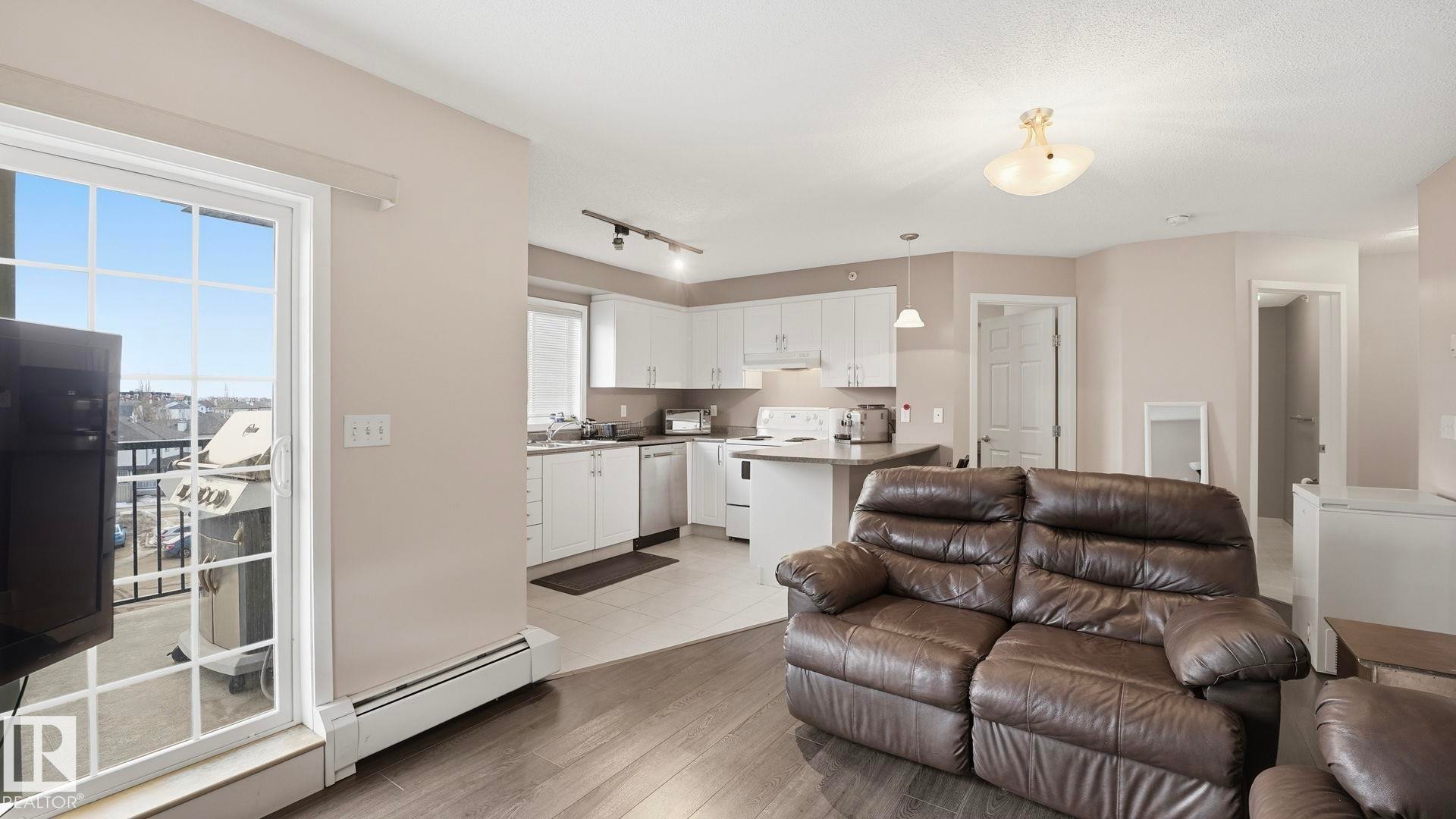 Living area with a baseboard radiator, light wood finished floors, and track lighting - 401 636 Mcallister Loop, Edmonton, AB - Indoor