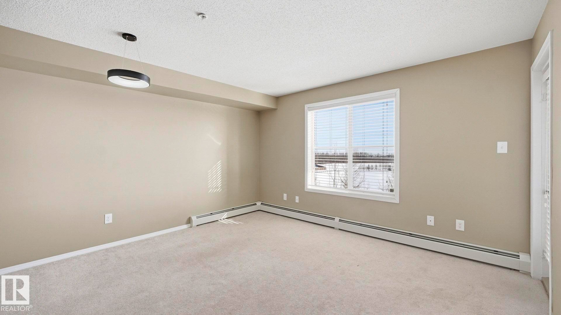 Spare room featuring light carpet, a textured ceiling, and a baseboard heating unit - 319 274 Mcconachie Drive, Edmonton, AB - Indoor Photo Showing Other Room