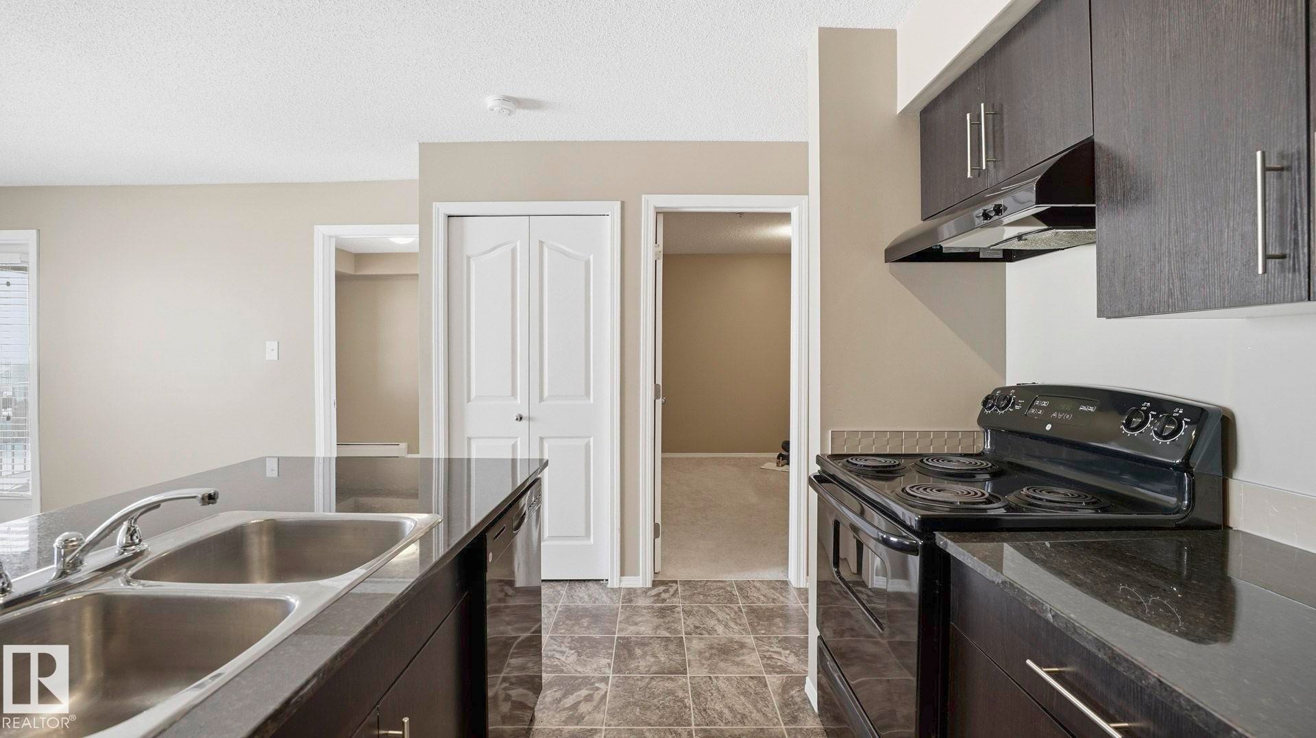 Kitchen with black appliances, a textured ceiling, dark wood finish cabinets, modern cabinets, and dark cabinets - 319 274 Mcconachie Drive, Edmonton, AB - Indoor Photo Showing Kitchen With Double Sink