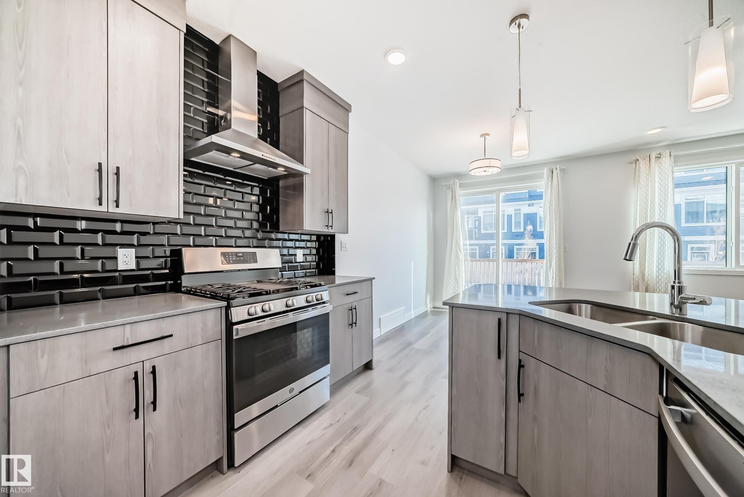 Kitchen with stainless steel appliances, hanging light fixtures, wall chimney exhaust hood, backsplash, and light stone counters - 2282 Chokecherry Close, Edmonton, AB - Indoor Photo Showing Kitchen With Double Sink With Upgraded Kitchen