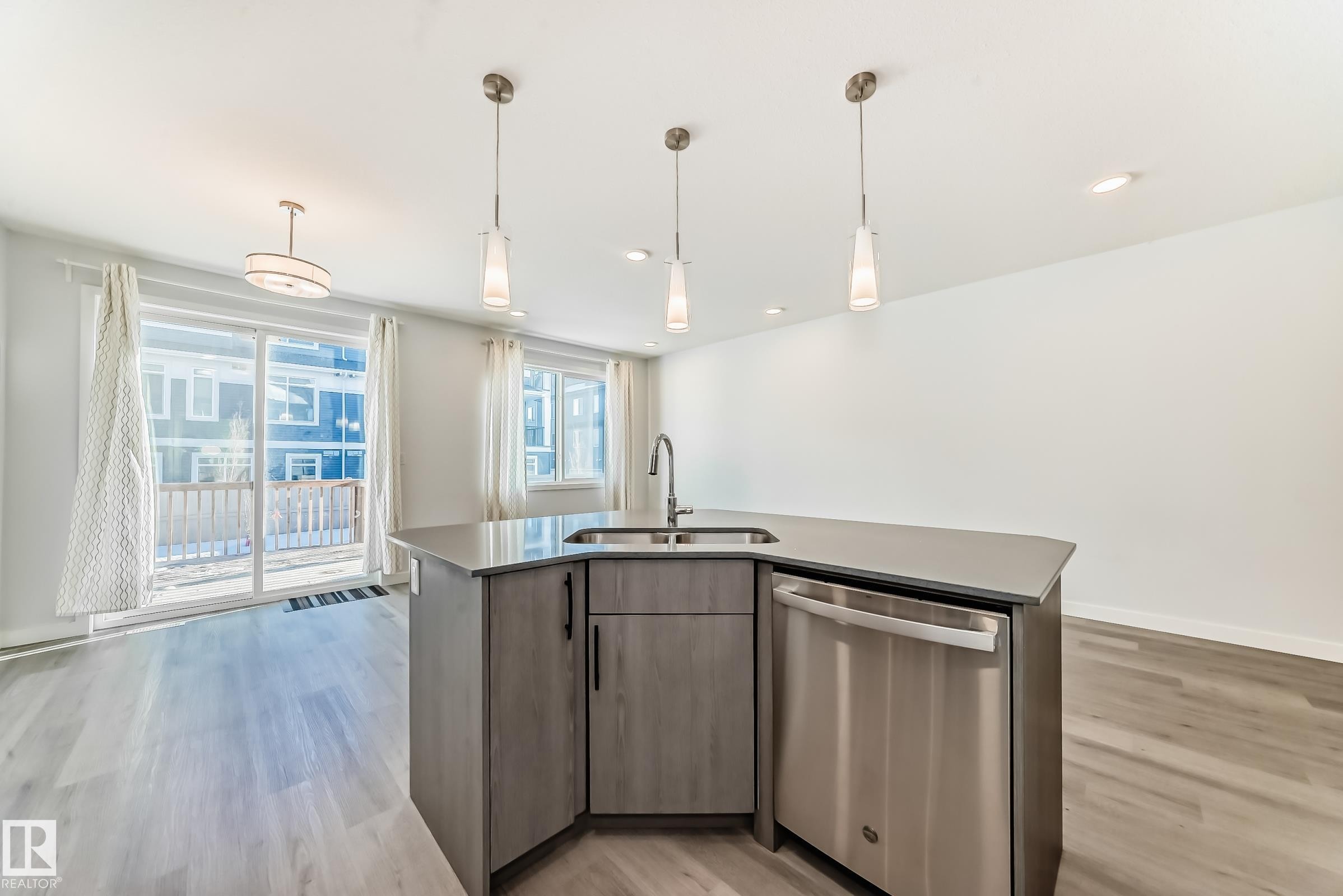 Kitchen featuring dishwasher, decorative light fixtures, light wood-style flooring, and a kitchen island with sink - 2282 Chokecherry Close, Edmonton, AB - Indoor Photo Showing Kitchen With Double Sink