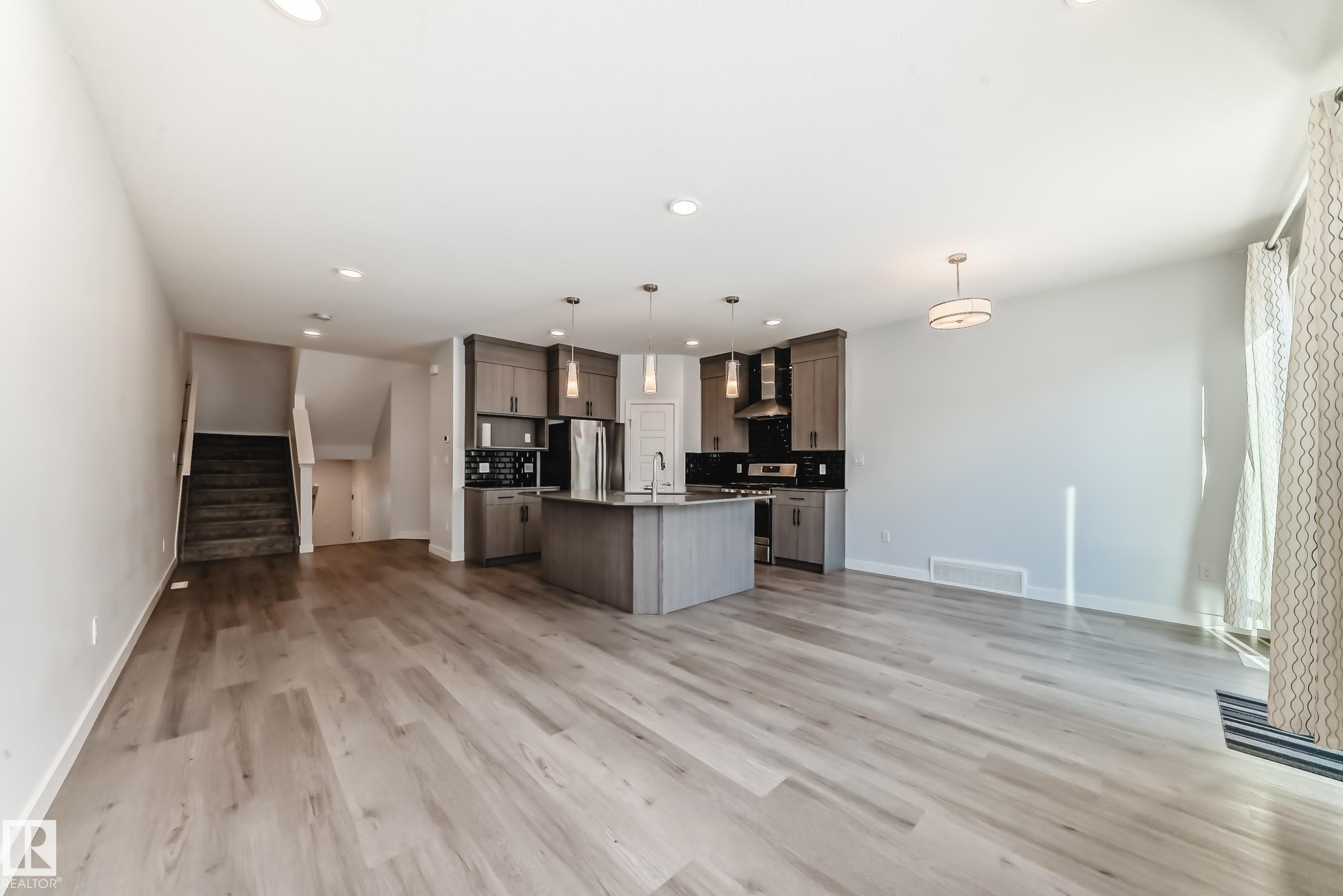 Kitchen featuring open floor plan, hanging light fixtures, an island with sink, stainless steel appliances, and wall chimney range hood - 2282 Chokecherry Close, Edmonton, AB - Indoor Photo Showing Kitchen