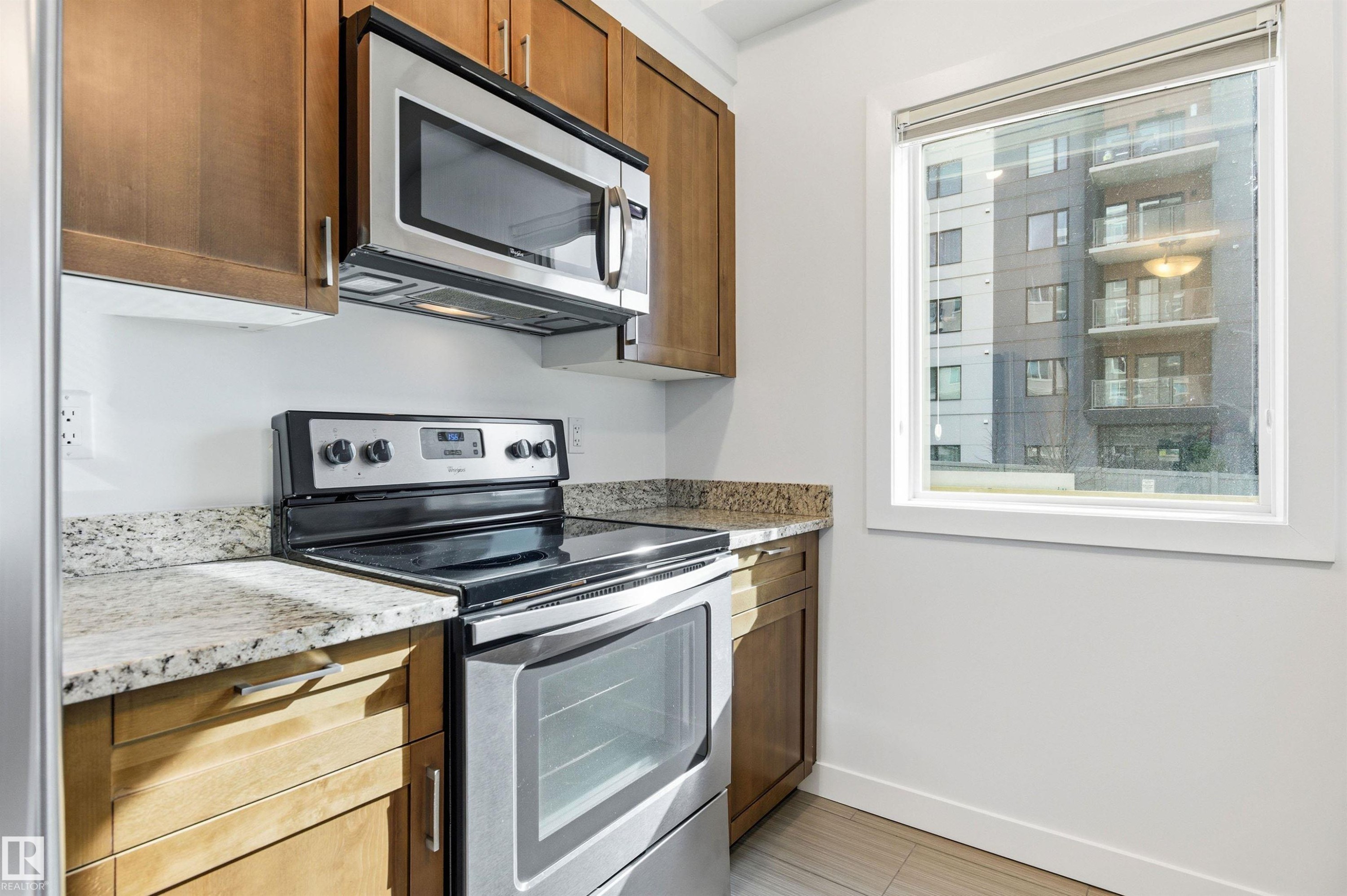 Kitchen with stainless steel appliances, light stone countertops, and wood finish cabinetry - 106 1238 Windermere Way, Edmonton, AB - Indoor Photo Showing Kitchen