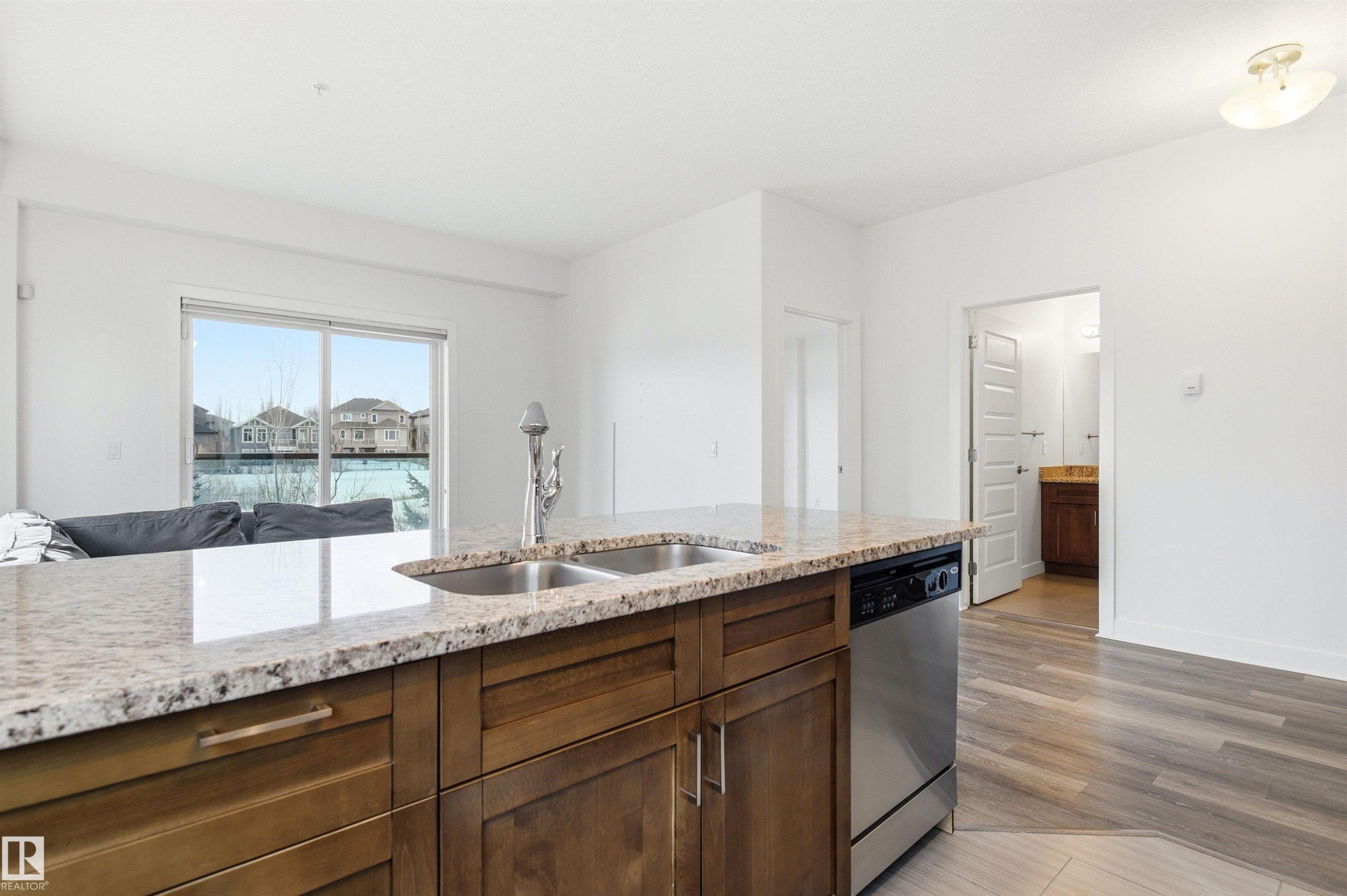Kitchen with dishwasher, light wood-style floors, light stone countertops, and open floor plan - 106 1238 Windermere Way, Edmonton, AB - Indoor Photo Showing Kitchen With Double Sink