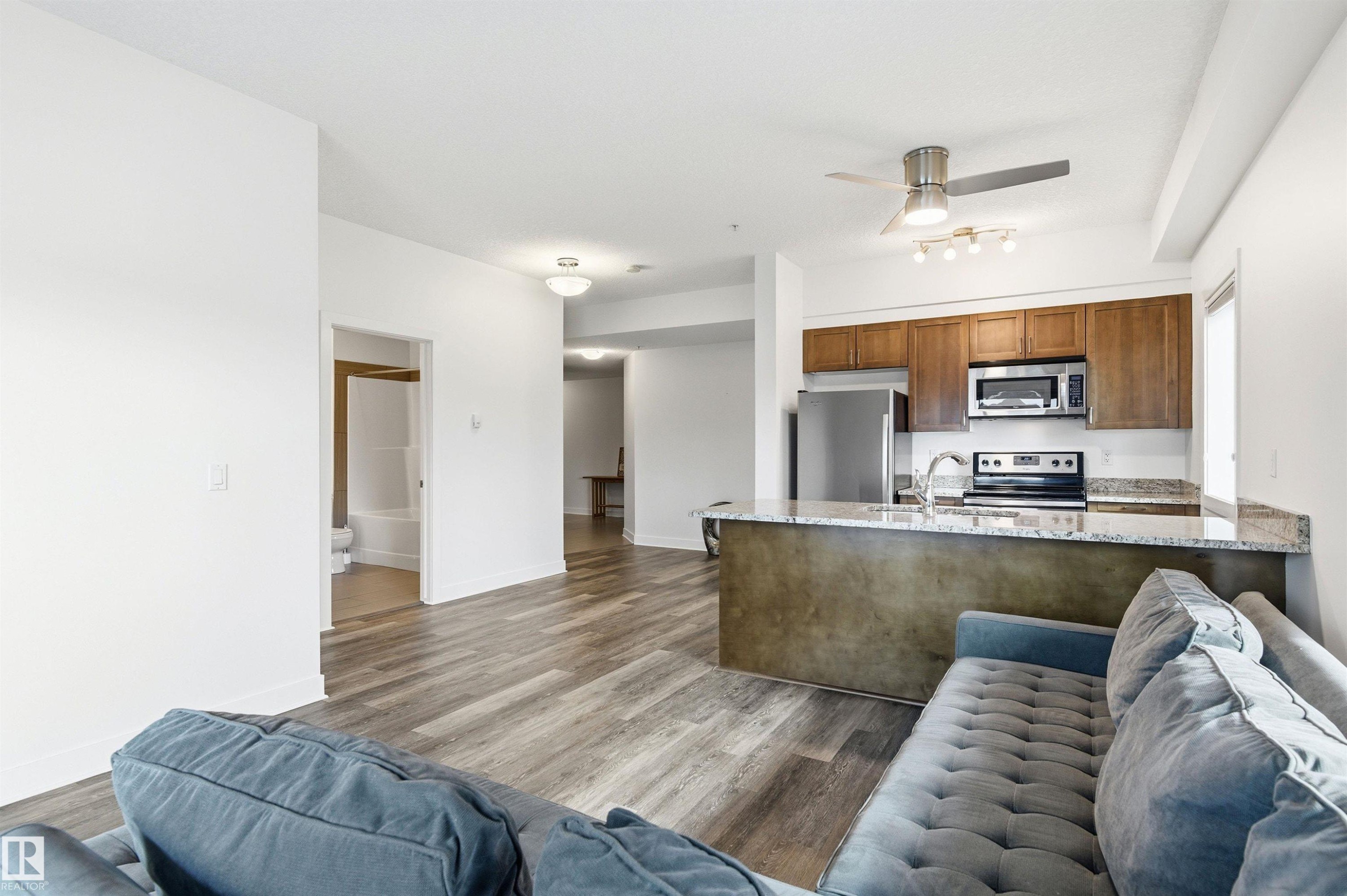 Kitchen with a peninsula, light stone counters, open floor plan, stainless steel appliances, and dark wood-style flooring - 106 1238 Windermere Way, Edmonton, AB - Indoor