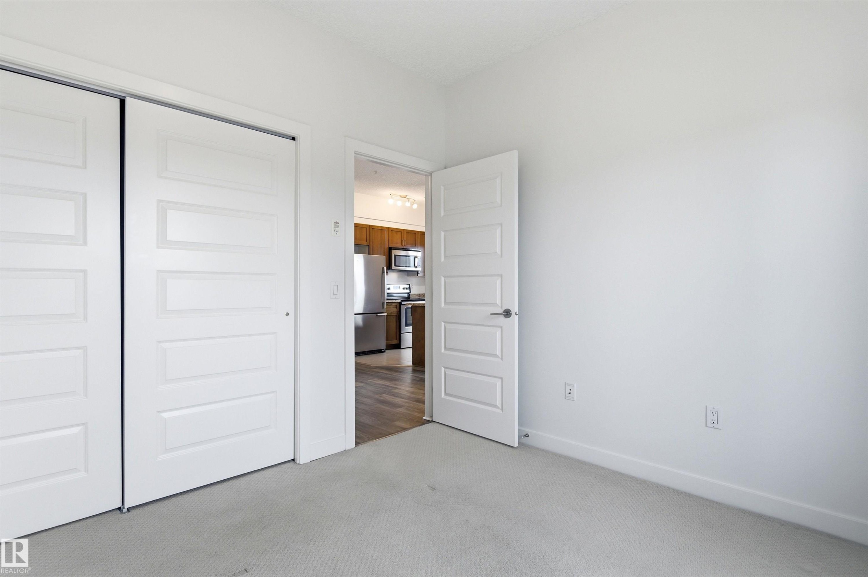 Unfurnished bedroom featuring light colored carpet, a closet, and freestanding refrigerator - 106 1238 Windermere Way, Edmonton, AB - Indoor Photo Showing Other Room