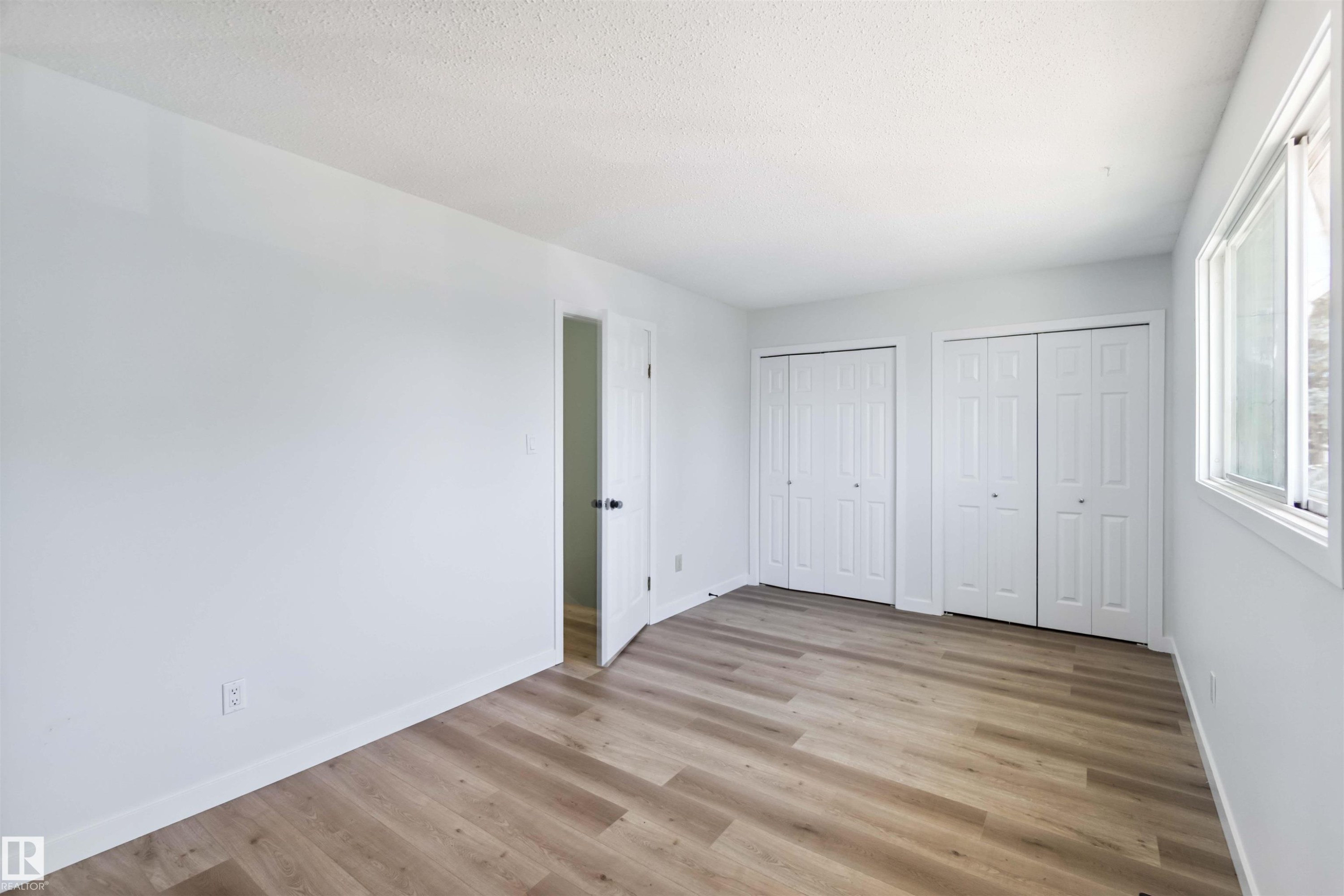 Unfurnished bedroom featuring two closets, light wood-style flooring, and a textured ceiling - 1096 Millbourne Road E, Edmonton, AB - Indoor Photo Showing Other Room