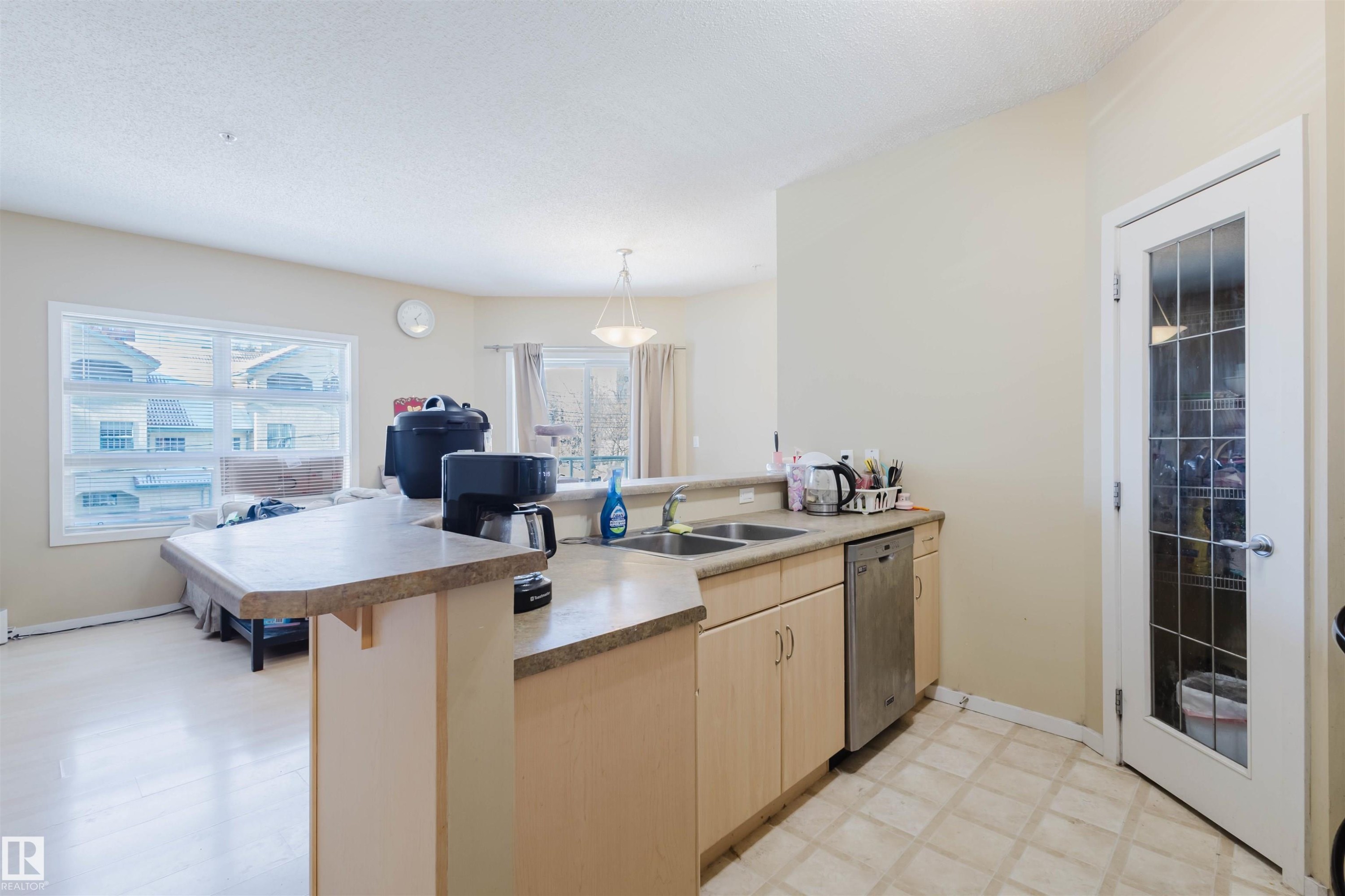 Kitchen with a peninsula, light wood finish cabinets, dishwasher, a kitchen breakfast bar, and light countertops - 207 9910 111 Street, Edmonton, AB - Indoor Photo Showing Kitchen With Double Sink