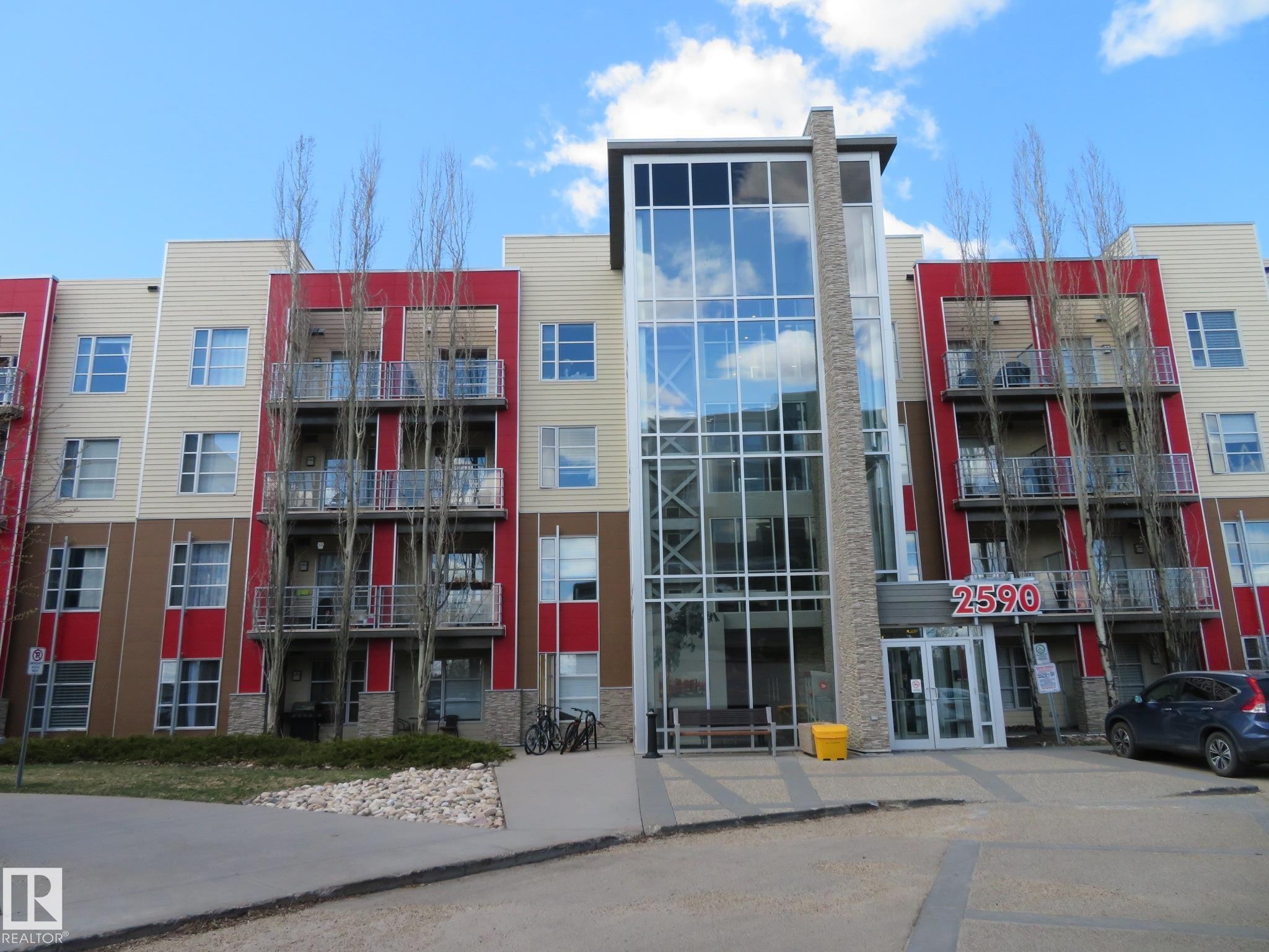 Modern five-story building featuring a prominent glass and stone-clad central entrance - 415 2590 Anderson Way, Edmonton, AB - Outdoor With Facade