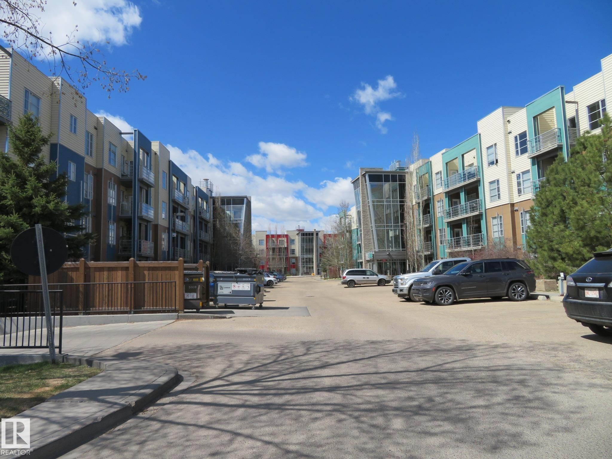 Multi-story residential buildings featuring varied exterior siding, private balconies with metal railings, large windows, and mature evergreen trees - 415 2590 Anderson Way, Edmonton, AB - Outdoor With Facade