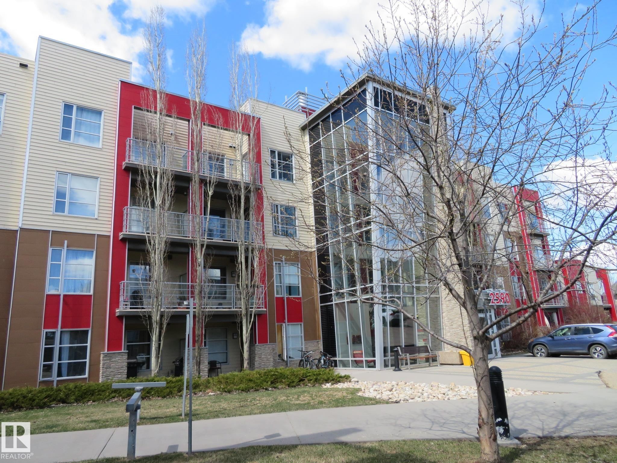 Modern multi-story building featuring a prominent glass-enclosed entrance - 415 2590 Anderson Way, Edmonton, AB - Outdoor With Facade