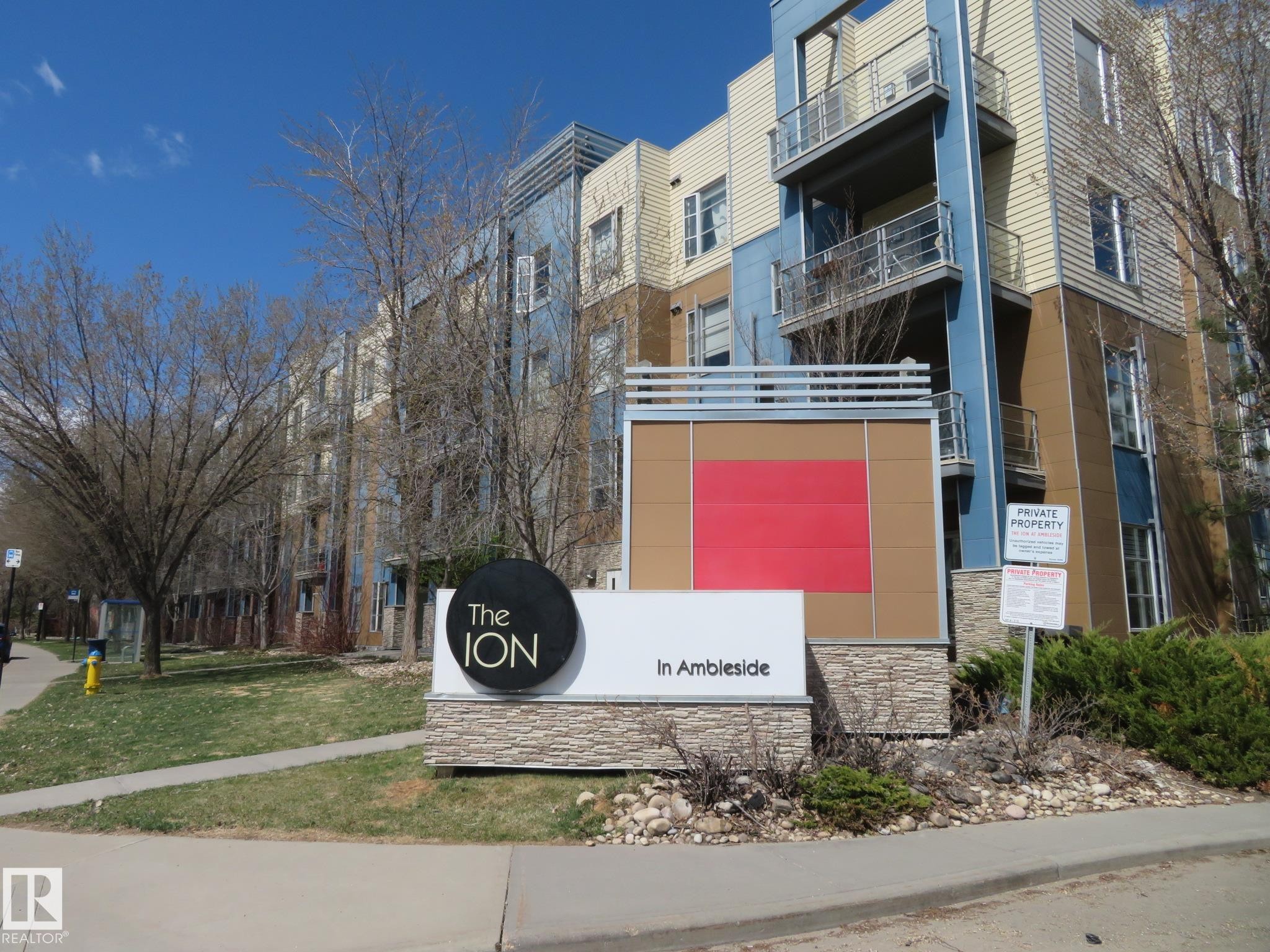 Multi-story building featuring balconies with metal railings, a stone base, and a contemporary mix of blue and beige siding - 415 2590 Anderson Way, Edmonton, AB - Outdoor