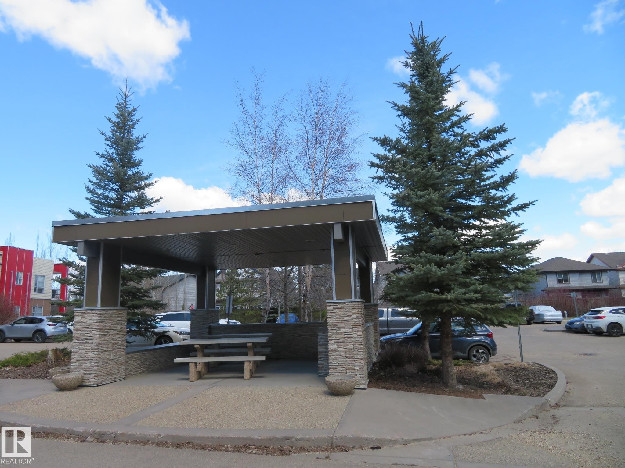 Covered outdoor gathering area featuring stone-clad columns and a sturdy wood picnic table - 415 2590 Anderson Way, Edmonton, AB - Outdoor