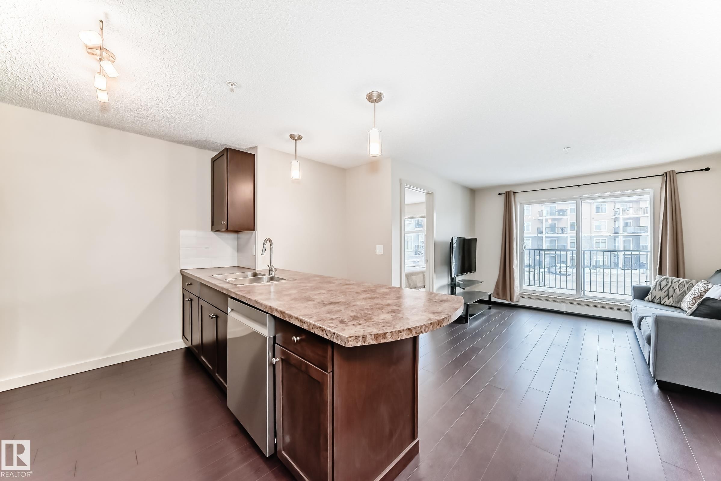 Kitchen featuring open floor plan, dark brown cabinets, a peninsula, light countertops, and stainless steel dishwasher - 229 6076 Schonsee Way, Edmonton, AB - Indoor