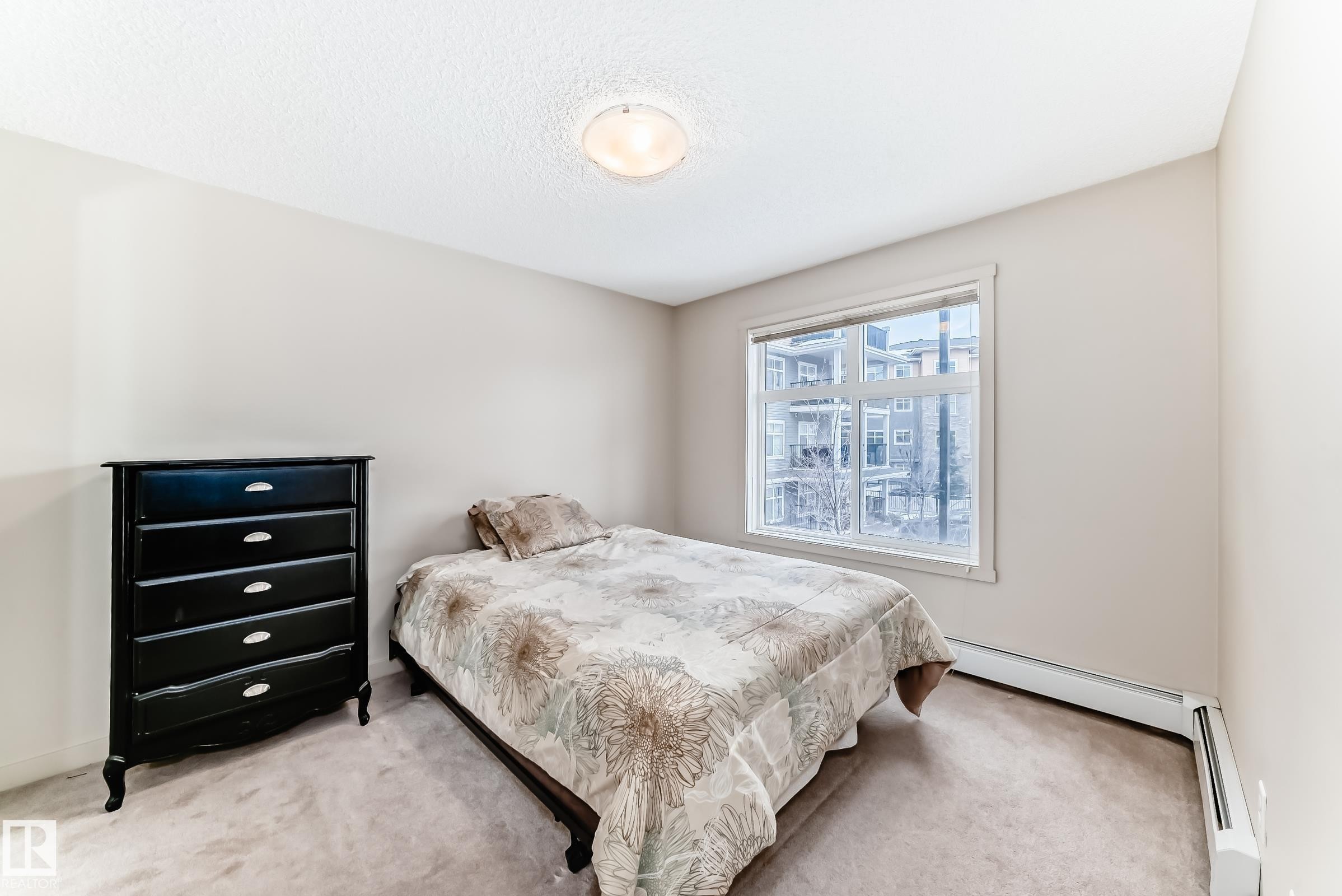Bedroom with carpet, a baseboard heating unit, and a textured ceiling - 229 6076 Schonsee Way, Edmonton, AB - Indoor Photo Showing Bedroom
