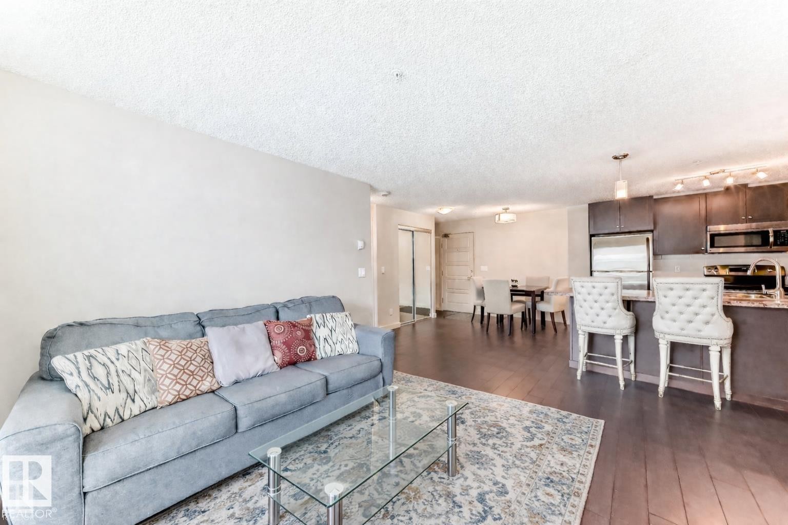 Living area with a textured ceiling and dark wood-style floors - 229 6076 Schonsee Way, Edmonton, AB - Indoor Photo Showing Living Room