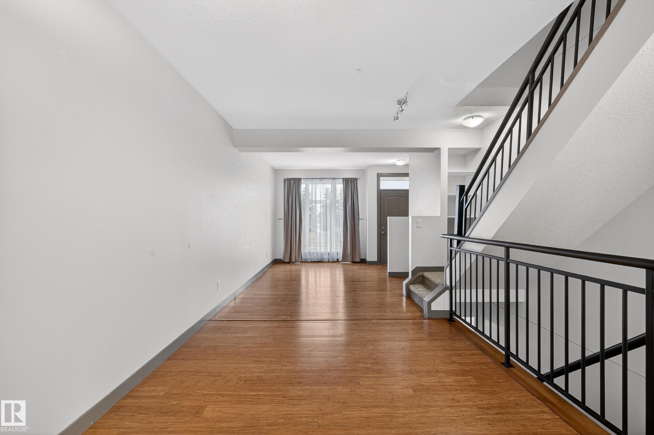 The property features warm hardwood flooring, white walls, and a staircase with a black metal railing - 1649 Cunningham Way, Edmonton, AB - Indoor Photo Showing Other Room