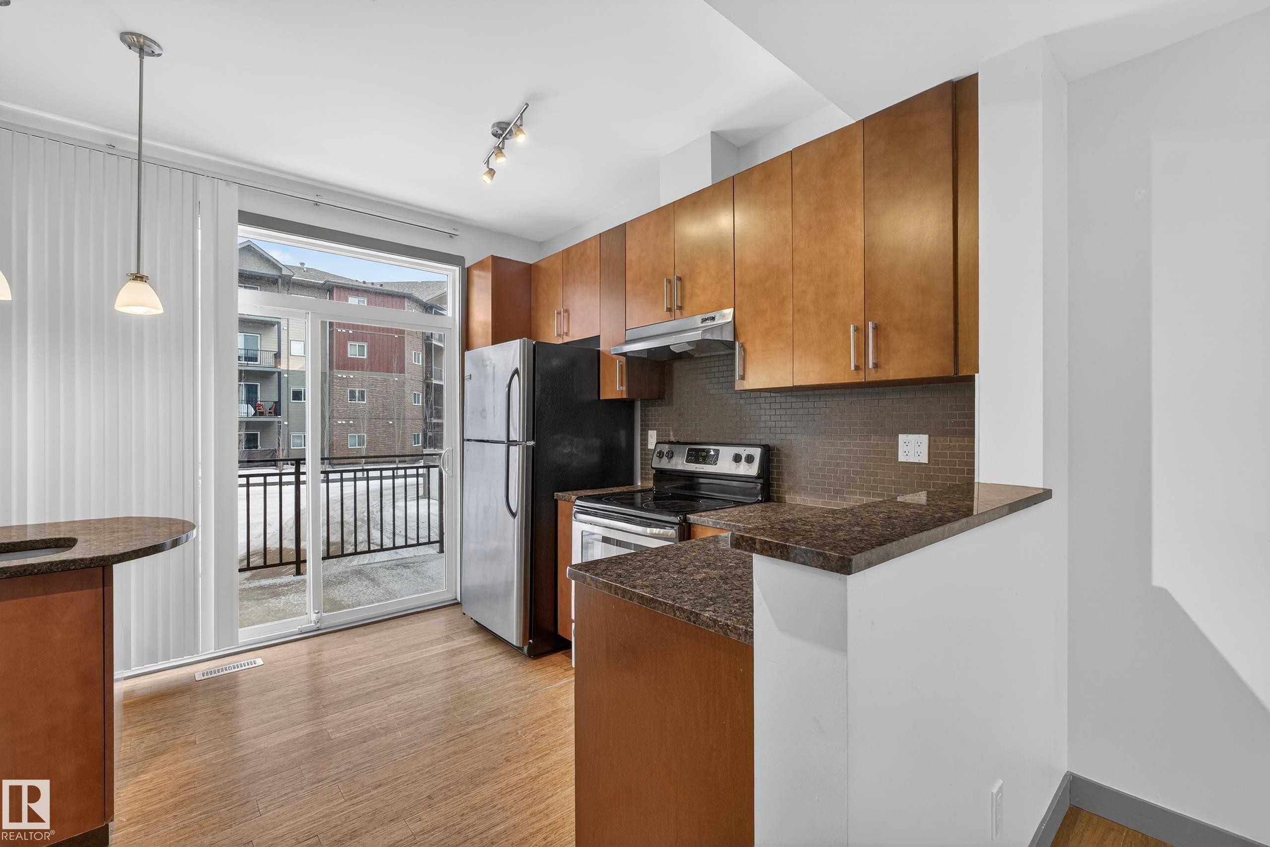 The property features a kitchen with wood cabinetry, dark countertops, and a tiled backsplash, and includes a refrigerator and stove - 1649 Cunningham Way, Edmonton, AB - Indoor Photo Showing Kitchen