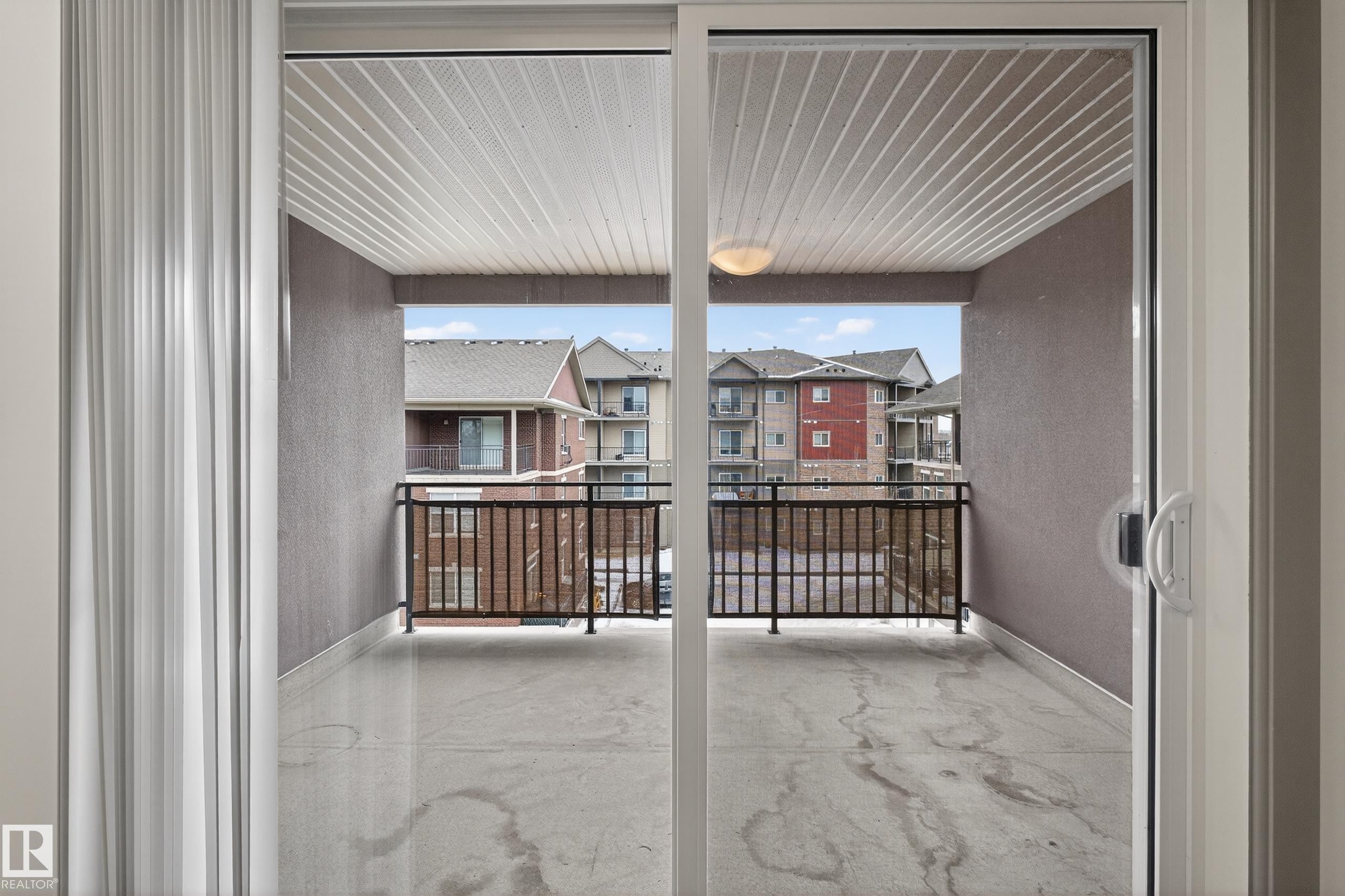 The property features a balcony with a concrete floor, dark railing, and a slatted ceiling, offering views of buildings - 1649 Cunningham Way, Edmonton, AB - Indoor Photo Showing Other Room