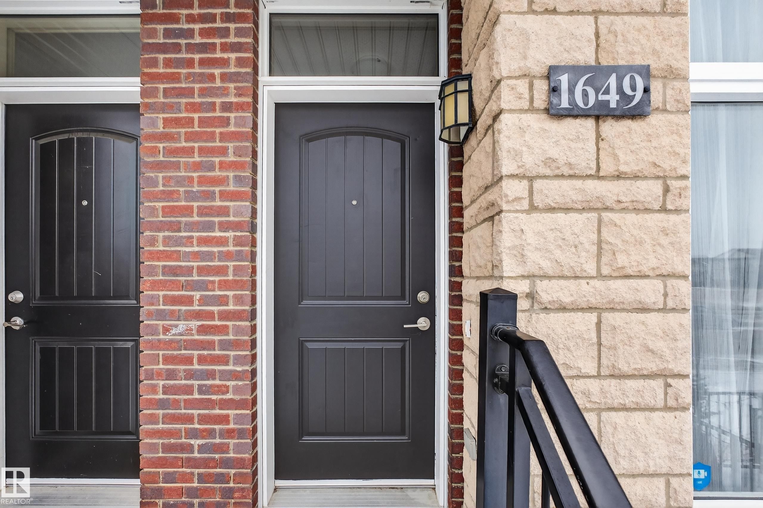 The property features a brick and stone facade, complemented by a dark entry door with a transom window above - 1649 Cunningham Way, Edmonton, AB - Outdoor With Exterior