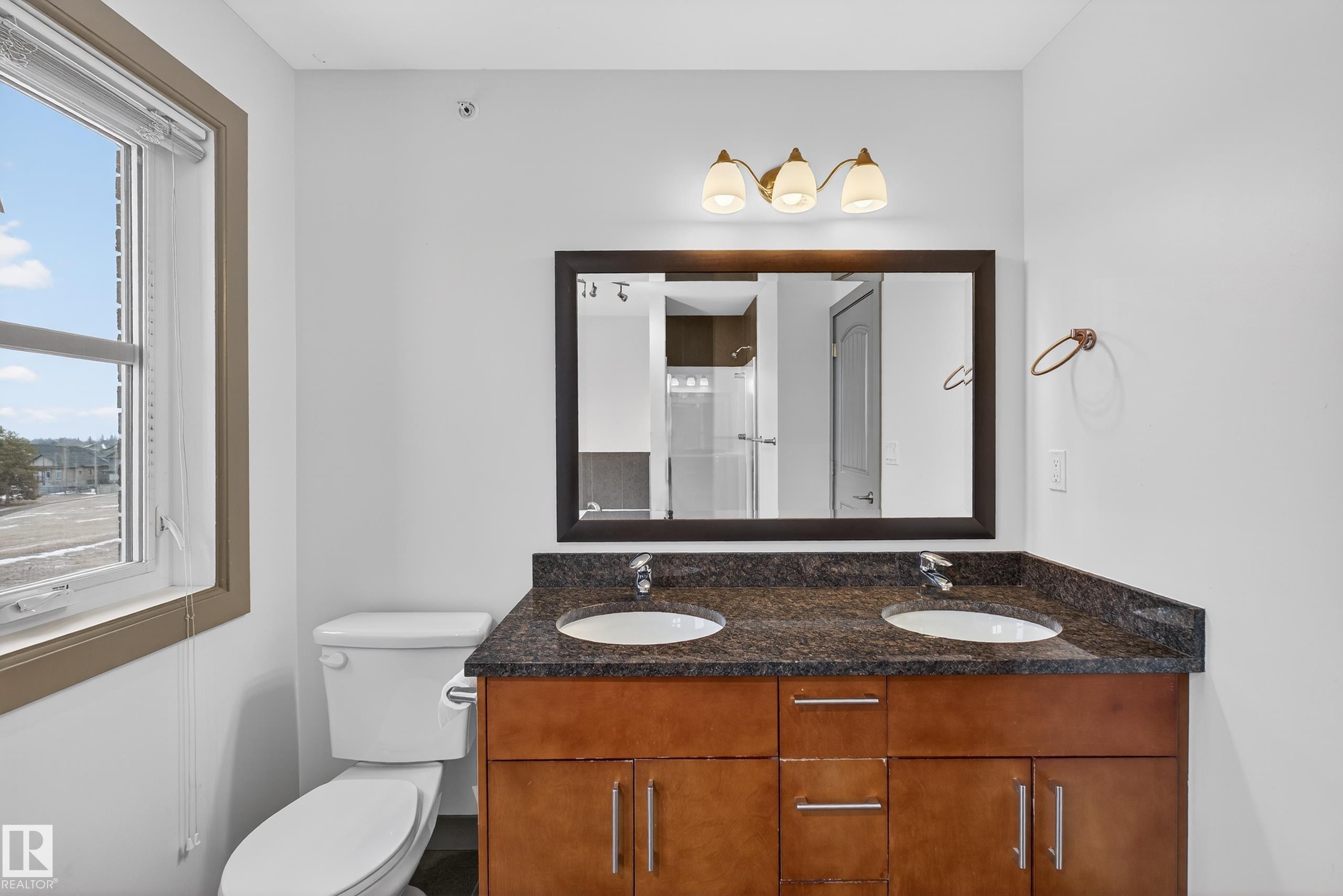 The bathroom features a double vanity with a dark granite countertop, two undermount sinks, and a framed mirror with an overhead light fixture - 1649 Cunningham Way, Edmonton, AB - Indoor Photo Showing Bathroom