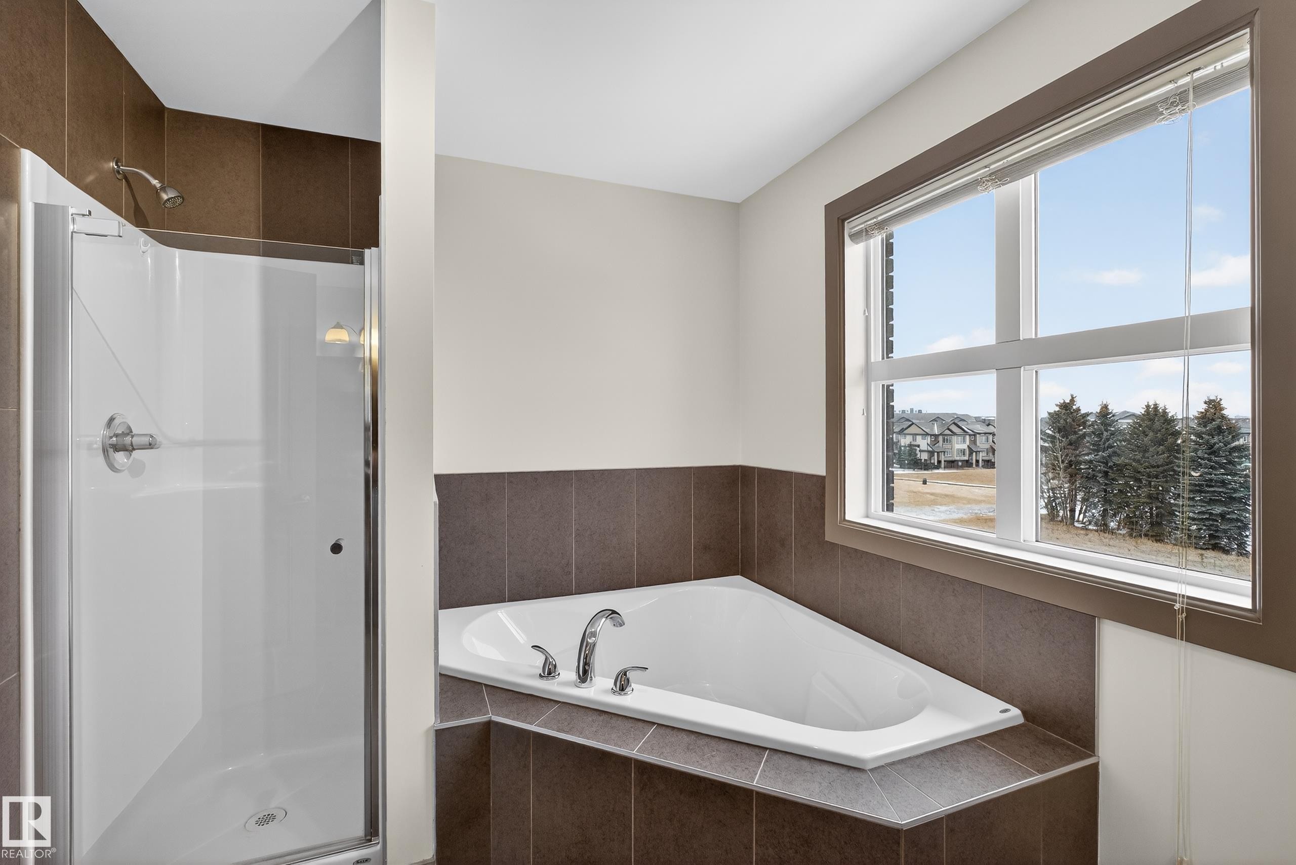 Bathroom featuring a built-in corner bathtub, a glass-enclosed shower, and a window providing natural light - 1649 Cunningham Way, Edmonton, AB - Indoor Photo Showing Bathroom