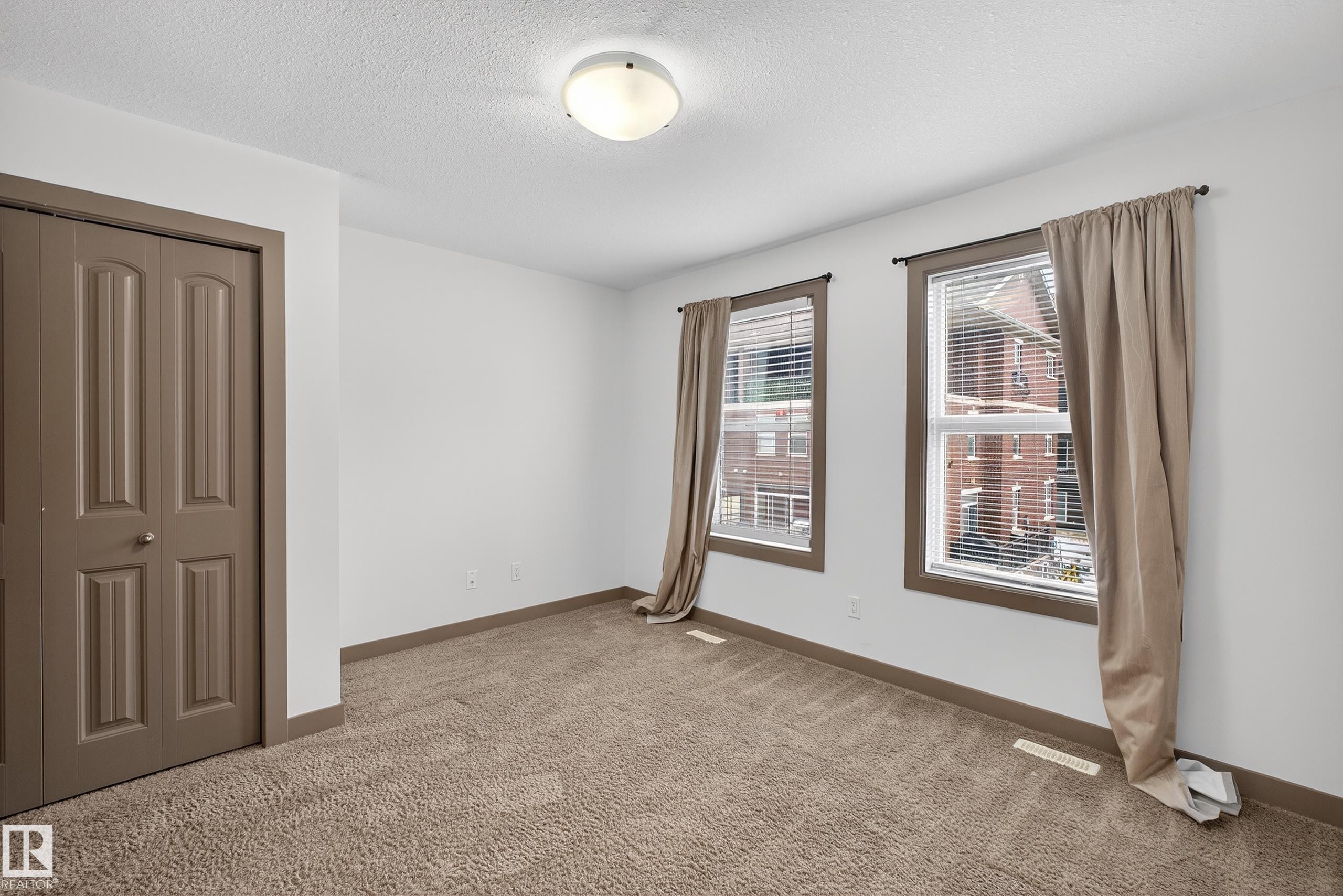 The property features a bright room with two windows, complete with blinds and curtains, offering views of the surrounding buildings - 1649 Cunningham Way, Edmonton, AB - Indoor Photo Showing Other Room