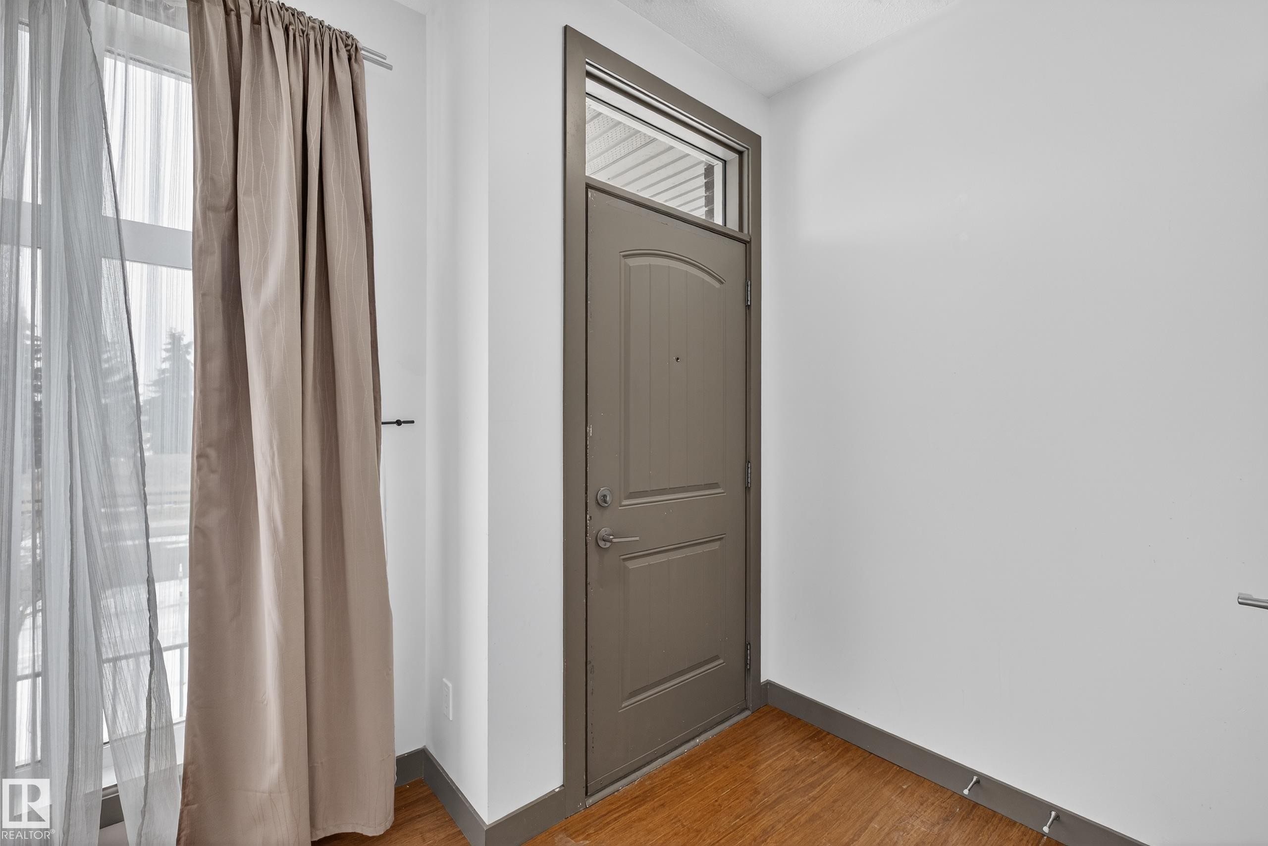 Entryway featuring a solid door with a transom window, hardwood flooring, and a window with sheer and blackout curtains - 1649 Cunningham Way, Edmonton, AB - Indoor Photo Showing Other Room