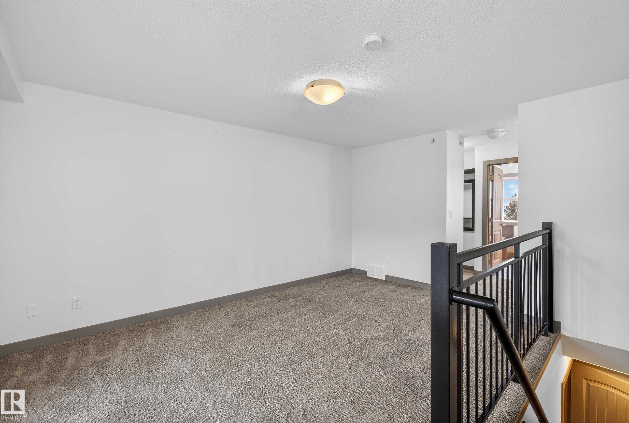 This room features wall-to-wall carpeting, a flush mount ceiling light fixture, and a dark-colored metal stair railing - 1649 Cunningham Way, Edmonton, AB - Indoor Photo Showing Other Room
