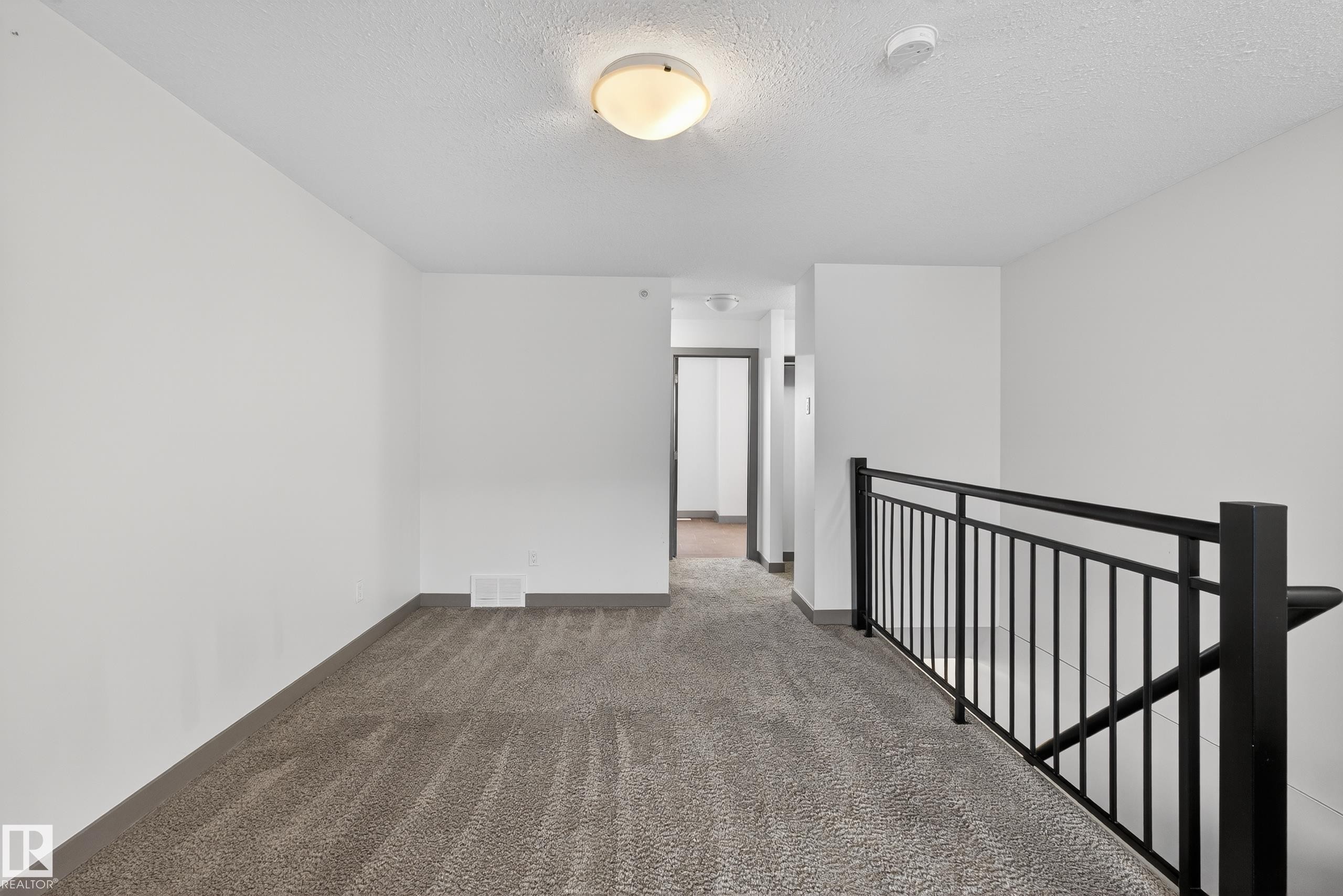 Open loft area featuring neutral-toned carpet flooring and a black metal railing - 1649 Cunningham Way, Edmonton, AB - Indoor Photo Showing Other Room